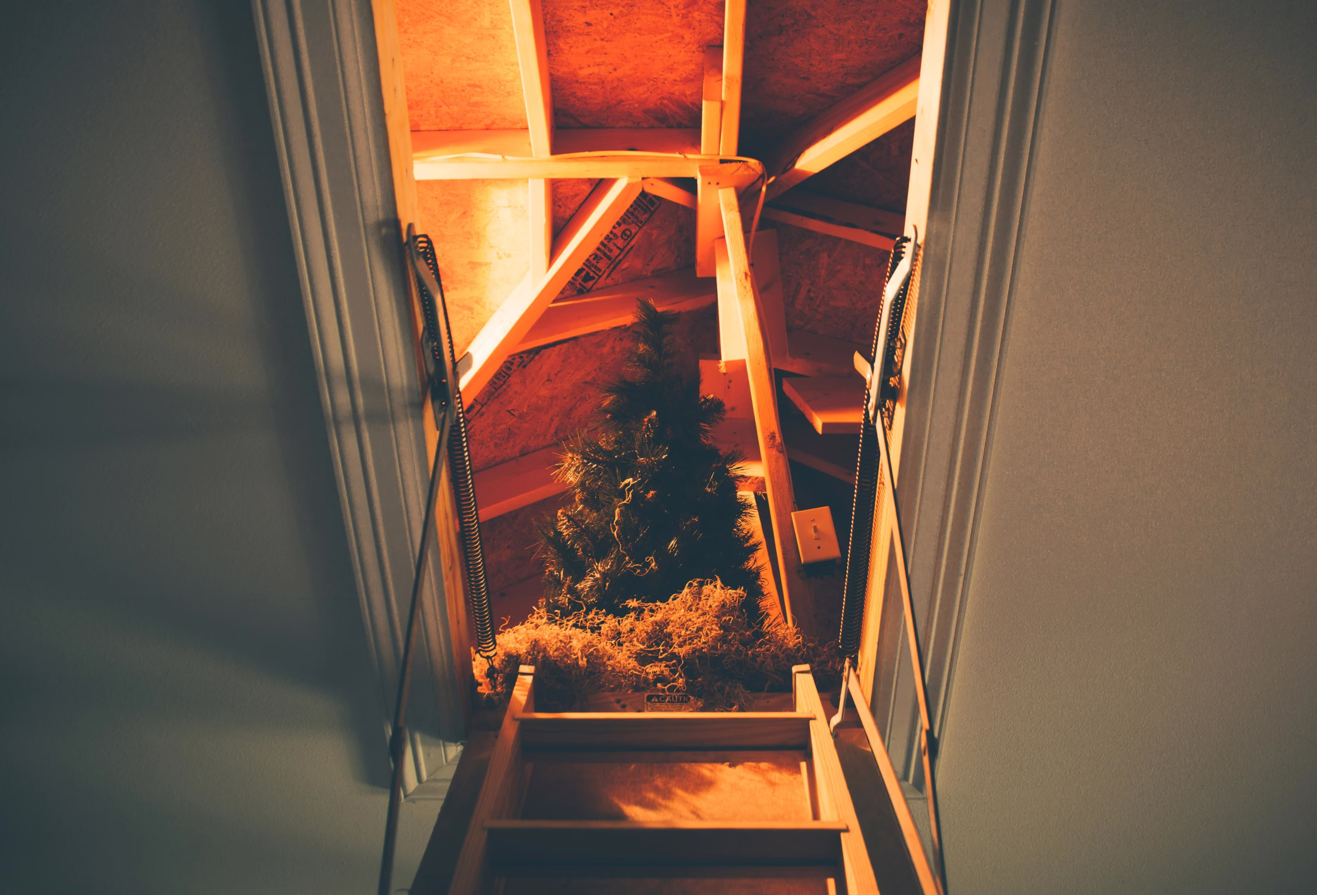 View through attic access hatch showing framing, ladder, and exposed insulation area where home air leaks commonly occur around the attic opening.