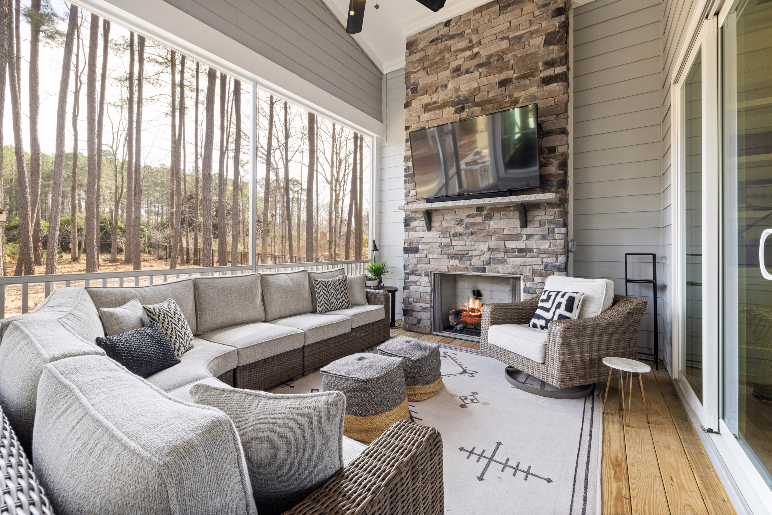 Screened in porch addition with sectional seating, stone fireplace, and wooded views, designed for comfort and connection by a remodeler College Station homeowners trust.