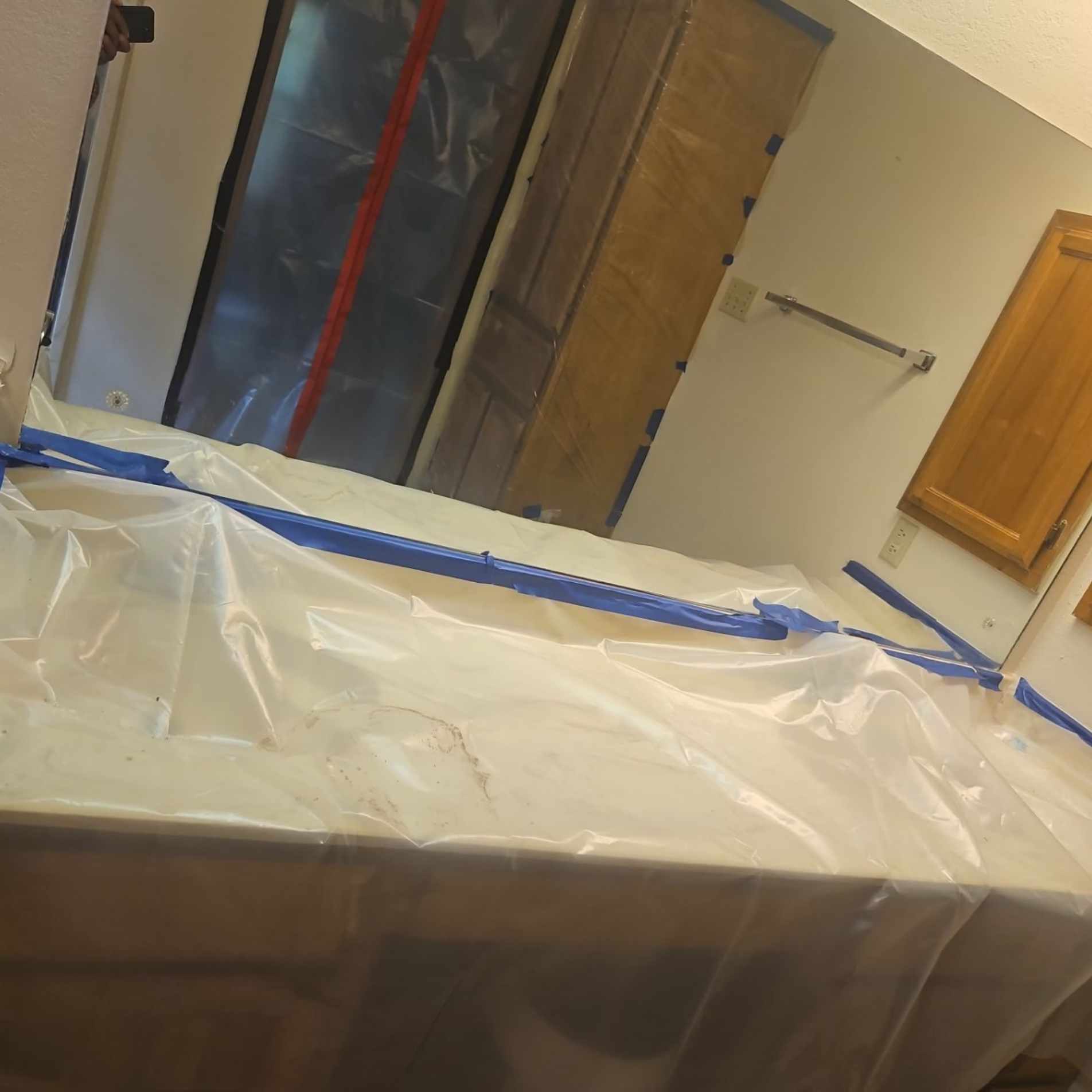 Bathroom countertops and existing fixtures covered with protective plastic sheeting and painter's tape during a home remodeling project.
