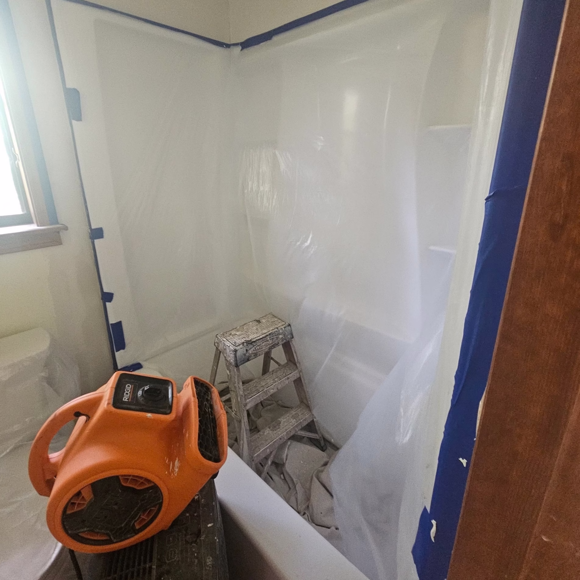 Temporary plastic dust barriers separating a bathroom construction area, with an air-moving fan positioned inside the work area.