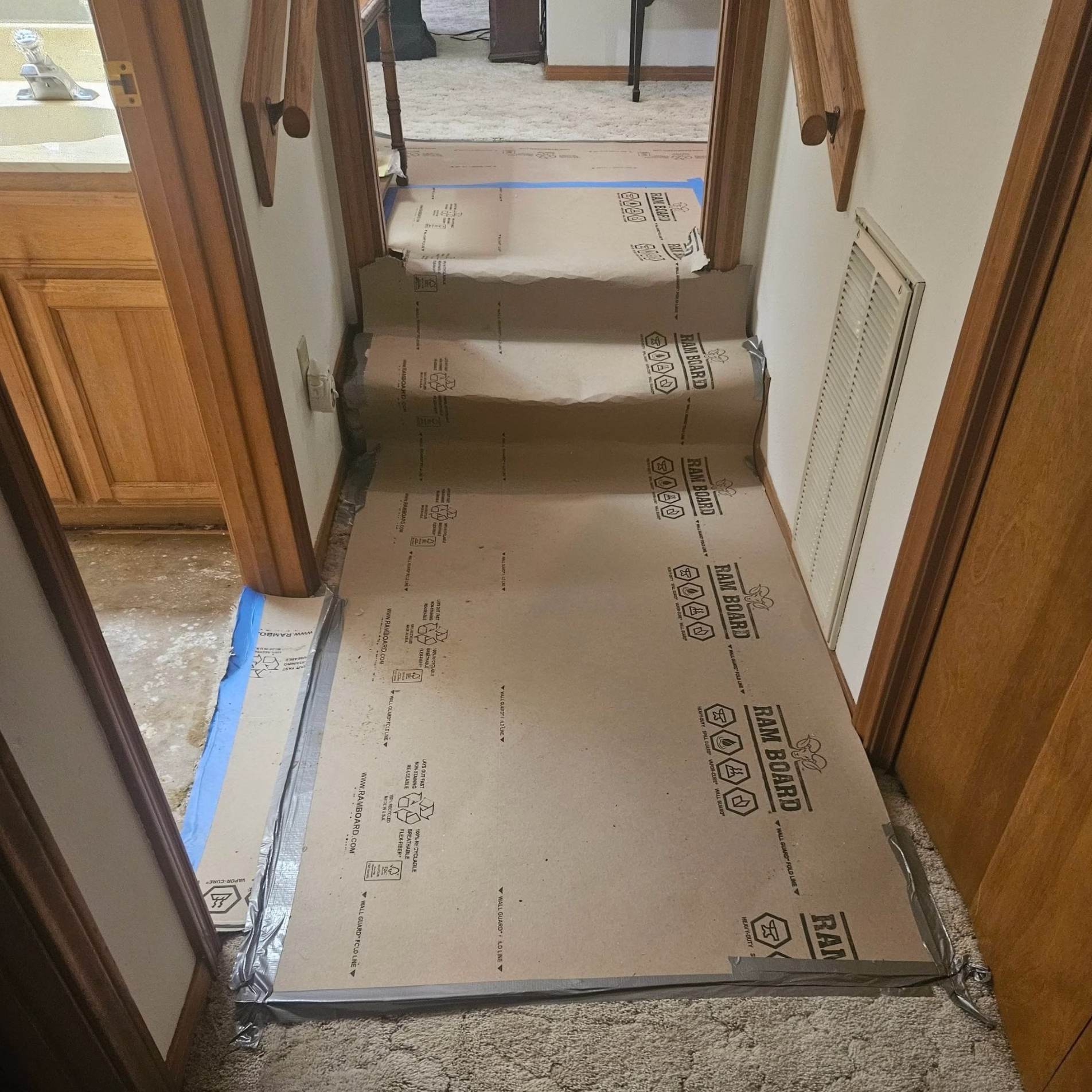 Temporary protective floorboards secured over a carpeted hallway and steps to protect existing flooring during home remodeling.