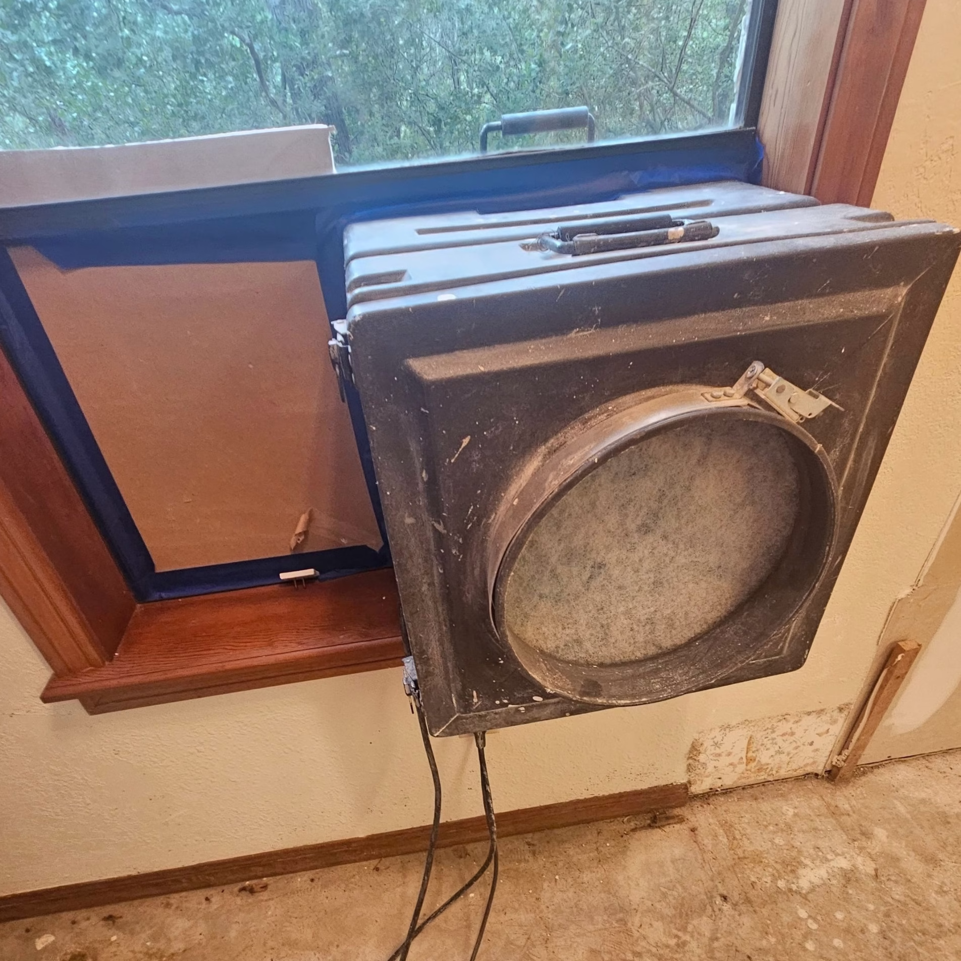 Construction air scrubber positioned against a window with a connected exhaust panel during an interior home remodeling project.
