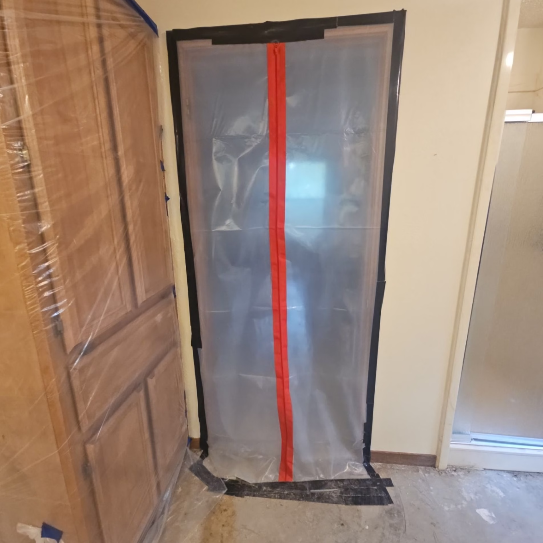 Temporary plastic dust containment doorway with a red zippered opening separating the construction area from the rest of the home.