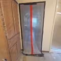 Temporary plastic dust containment doorway with a red zippered opening separating the construction area from the rest of the home.