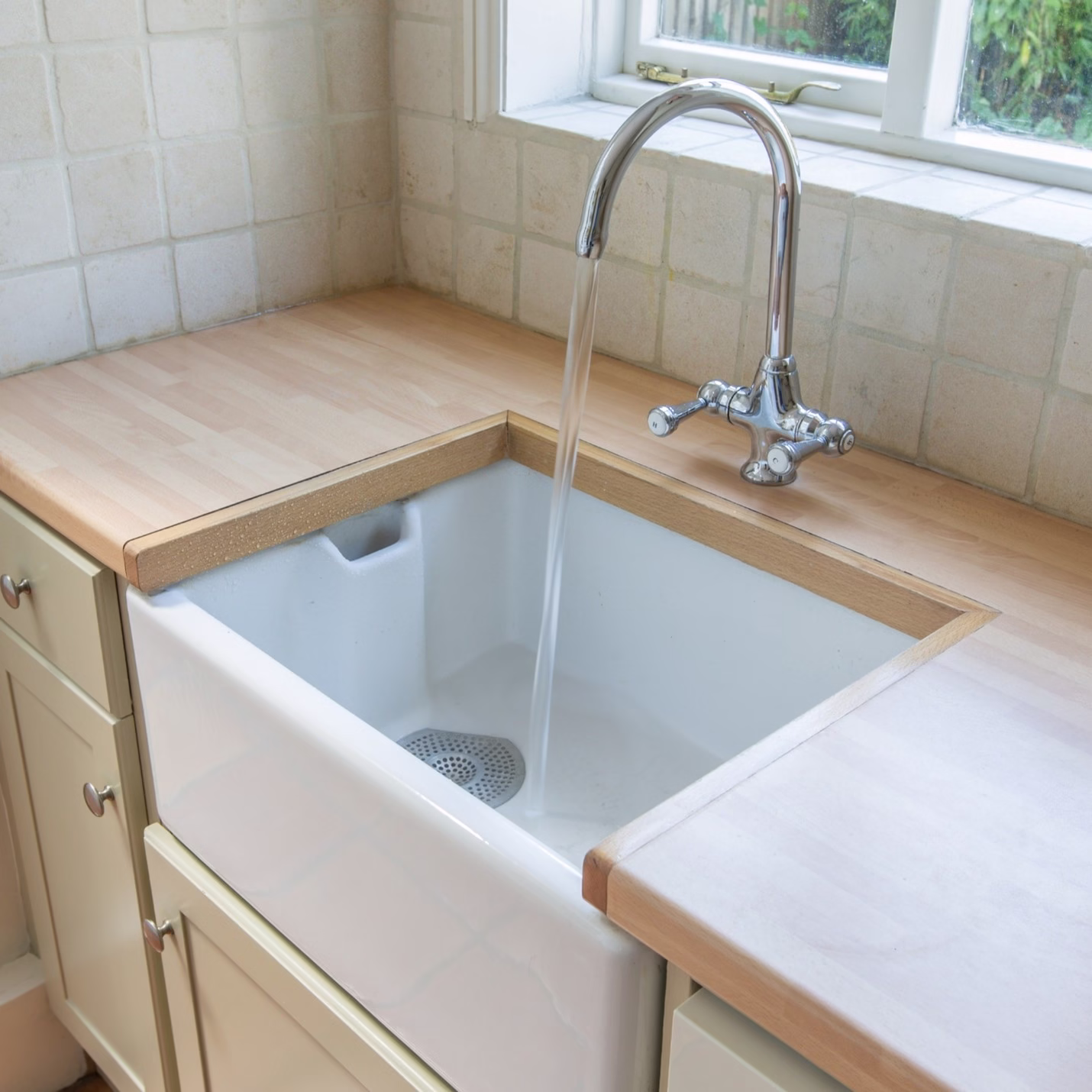 White farmhouse apron-front sink with butcher block countertops demonstrating types of kitchen sinks and important kitchen sink considerations for long-term function and maintenance