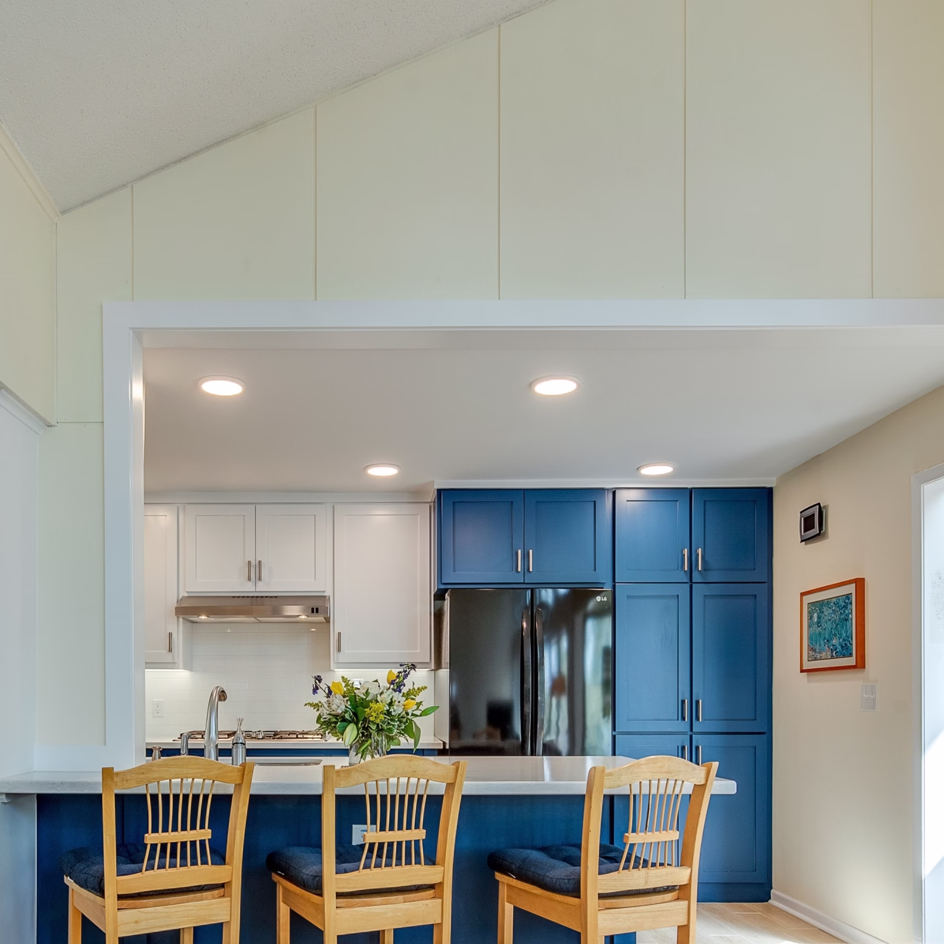 Remodeled College Station kitchen with enlarged opening, blue cabinetry, white countertops, and bar seating facing the family room.