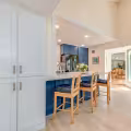 Finished kitchen bar with blue cabinetry, white countertop, seating, and new storage beside the enlarged opening.