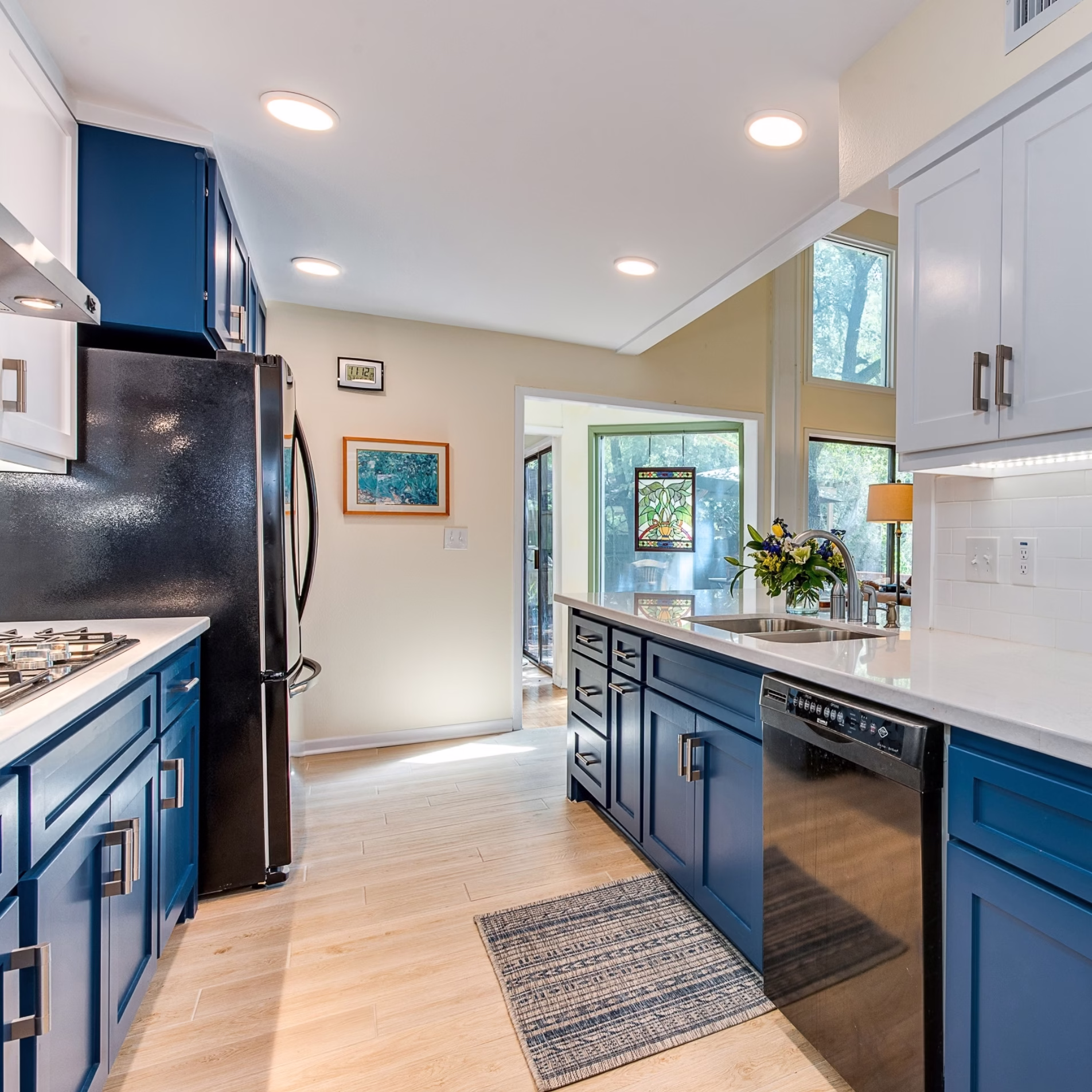 Remodeled kitchen with recessed ceiling lights, blue and white cabinetry, white countertops, and under-cabinet lighting.