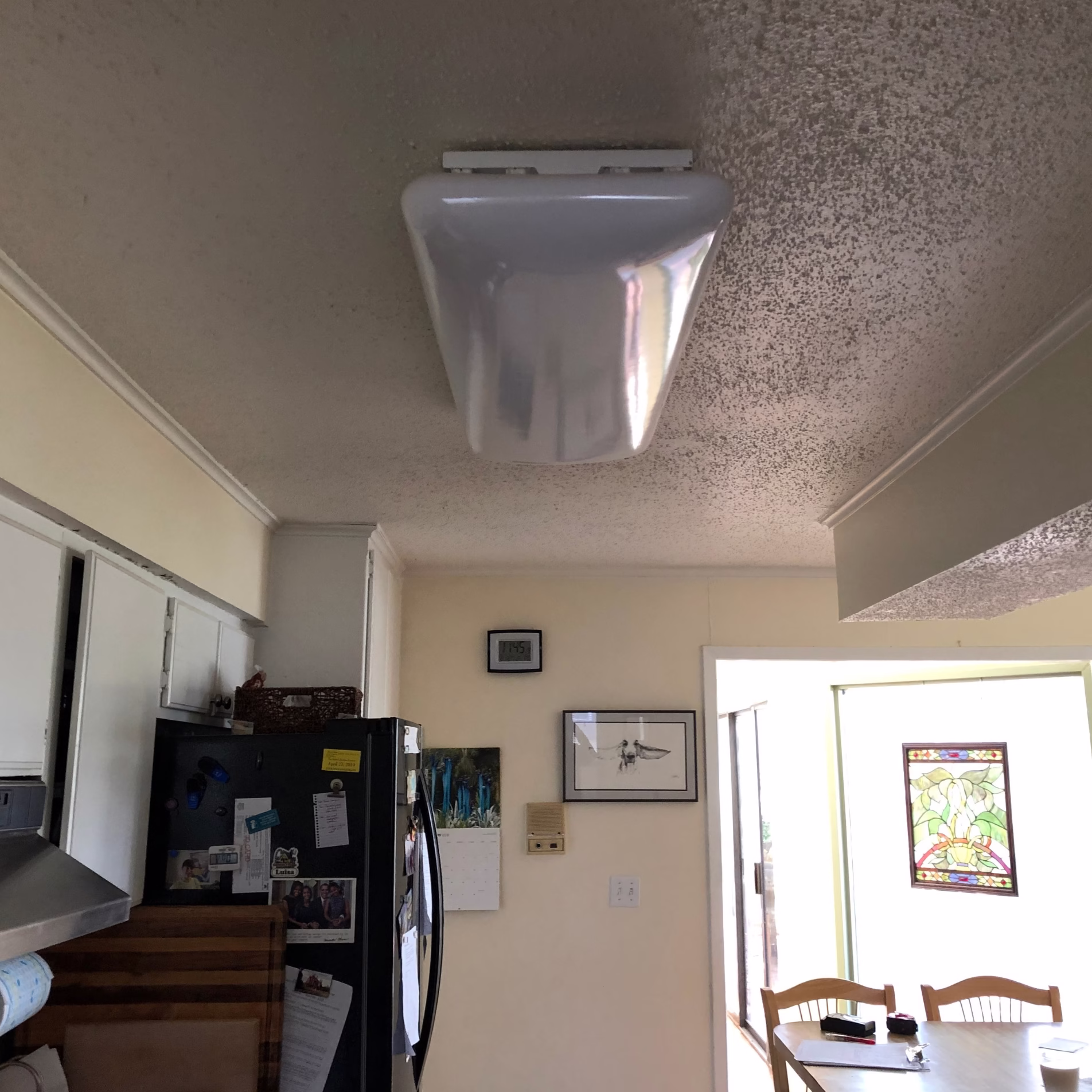 Kitchen before remodeling with a large surface-mounted ceiling light and original white cabinetry.