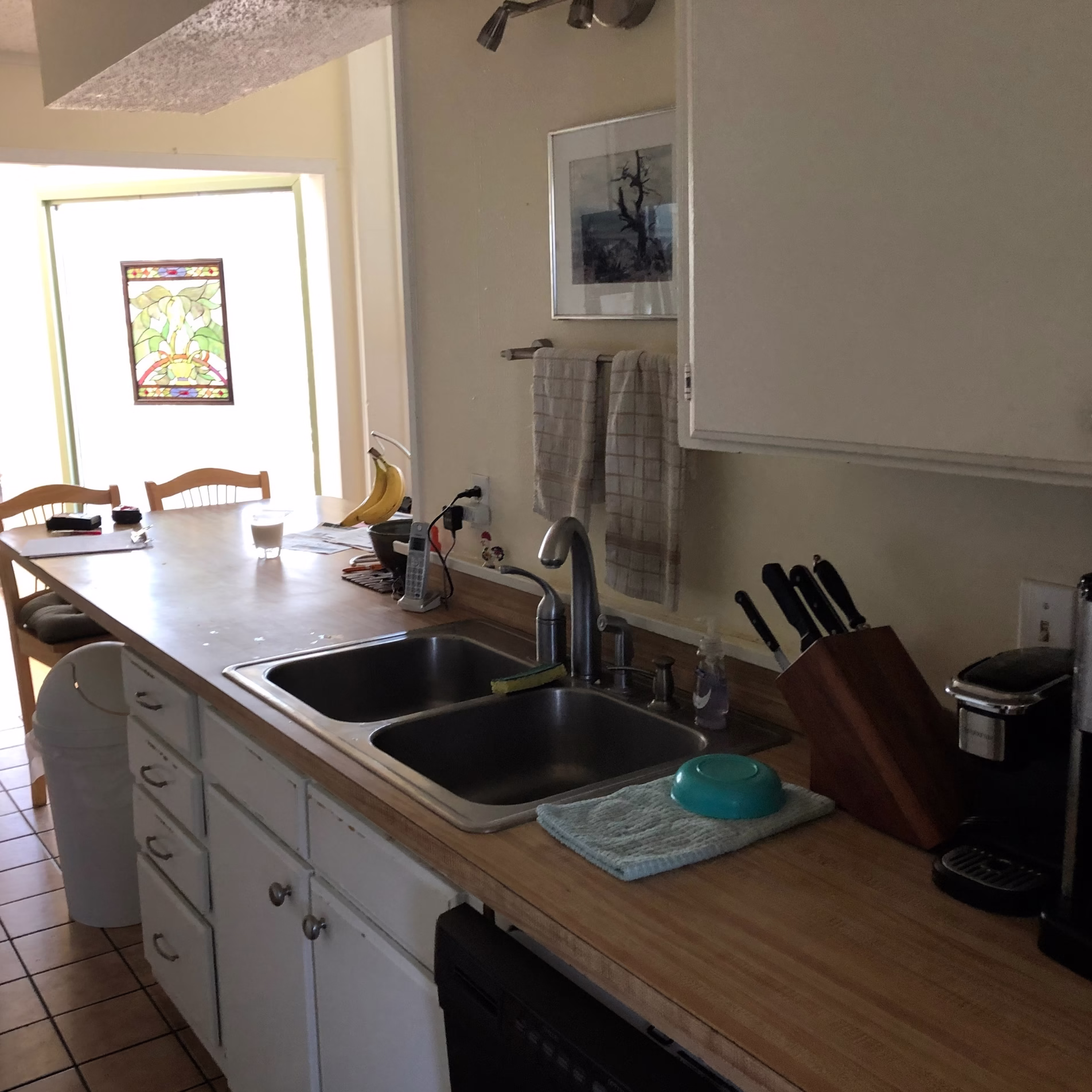 Kitchen sink area before remodeling with white cabinets, wood-look countertops, double-basin sink, and countertop appliances.