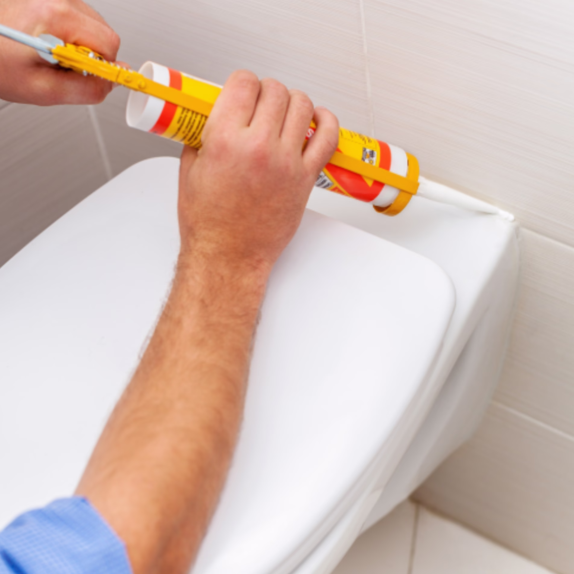 Applying fresh caulk along the joint between a bathtub and tiled bathroom wall