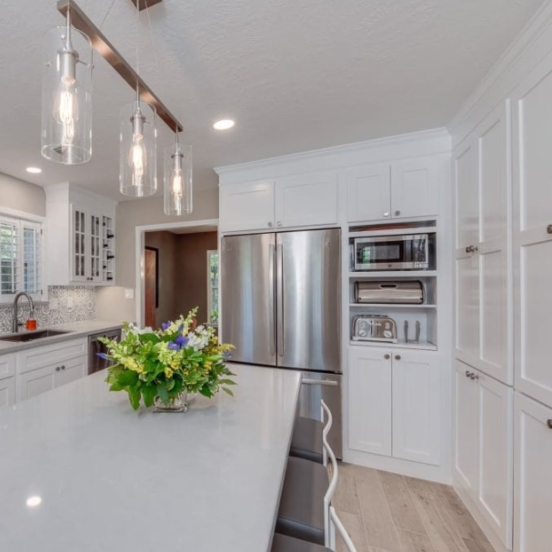 Remodeled kitchen featuring a large white island, floor-to-ceiling cabinetry, stainless steel refrigerator, and built-in microwave.