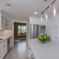 Completed kitchen remodel with a large white island, stainless steel appliances, tall storage cabinets, and wood-look flooring extending into the adjoining room.