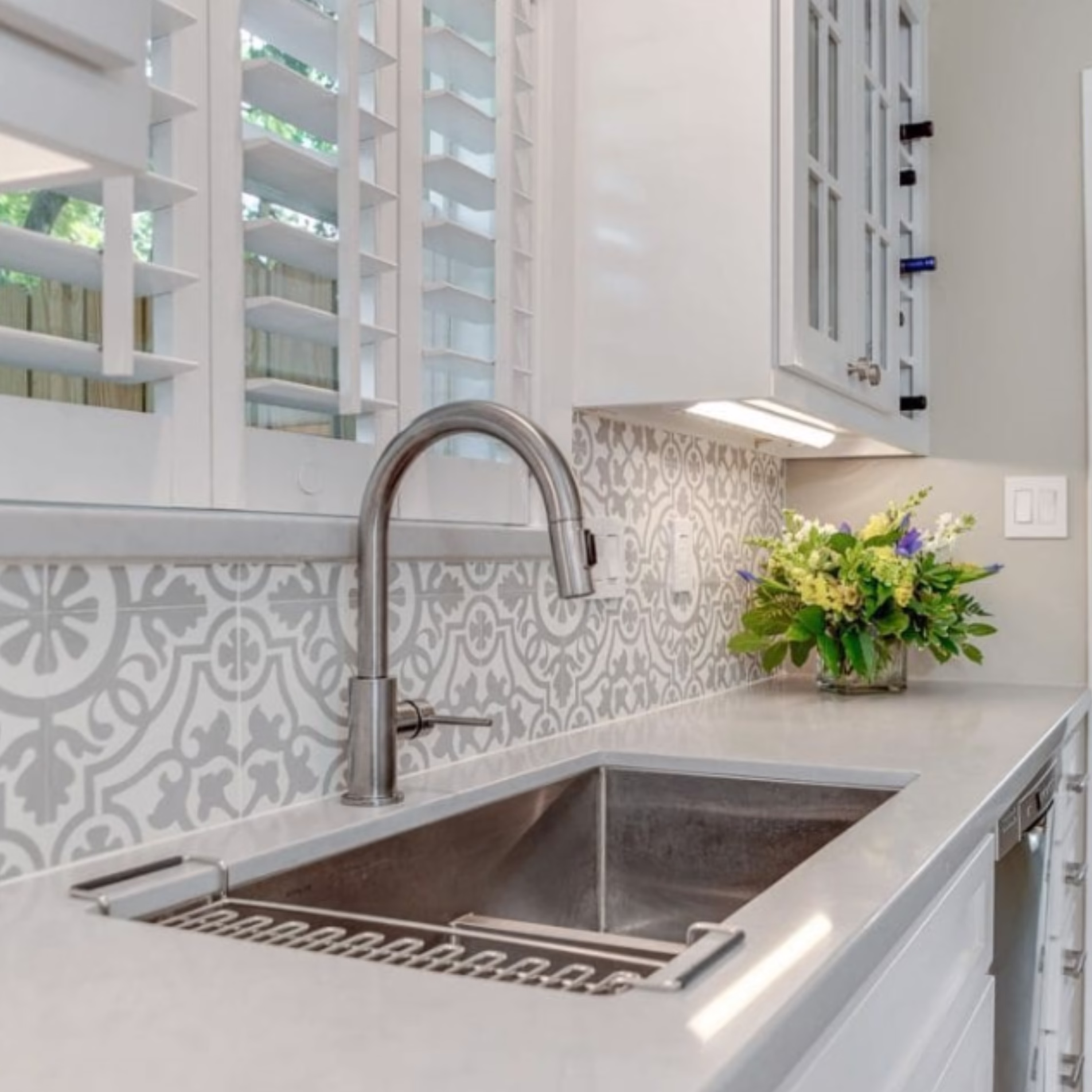 Italian-inspired kitchen remodel featuring a stainless steel undermount sink, patterned tile backsplash, white cabinetry, and a spacious central island.