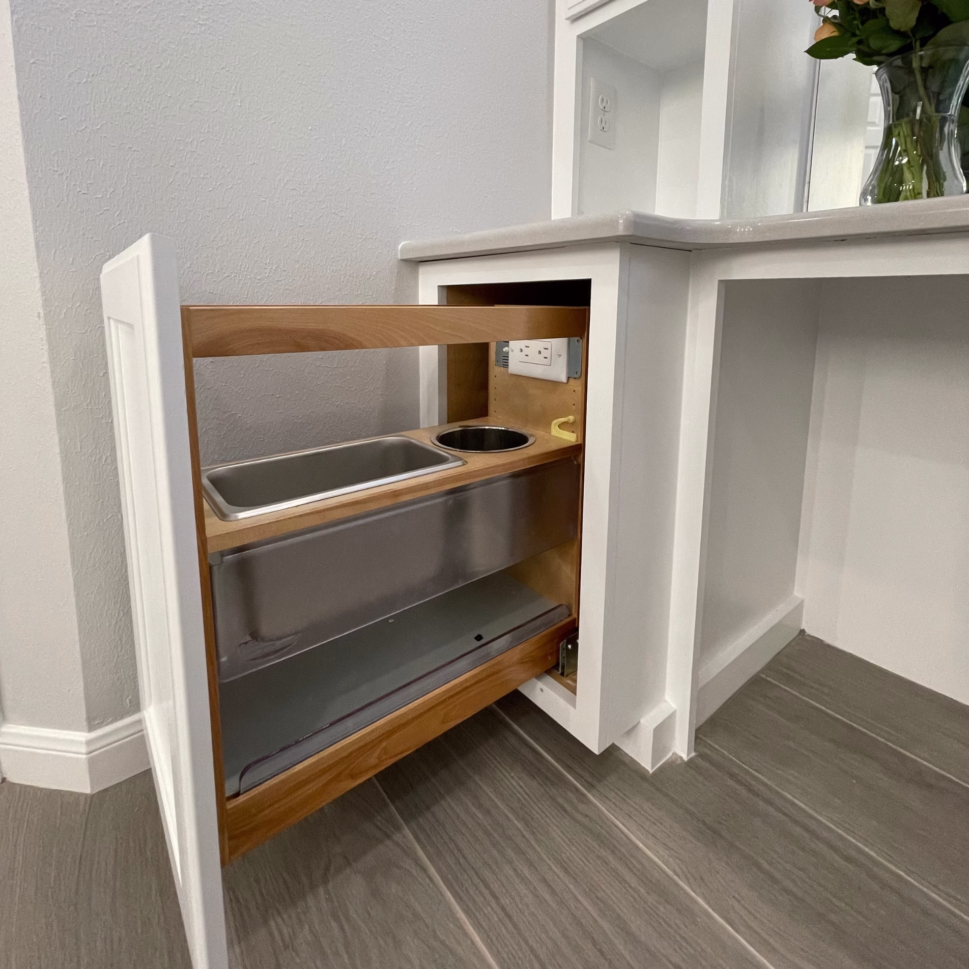 Pullout bathroom vanity storage with built-in compartments, metal canisters, and an electrical outlet for hair tools.