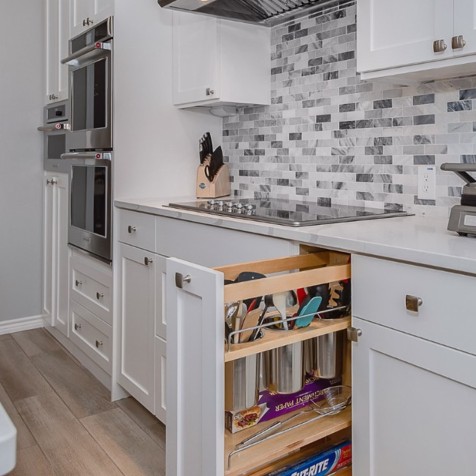 Pullout kitchen cabinet organizer storing utensils, cookware, foil, and other frequently used kitchen supplies.