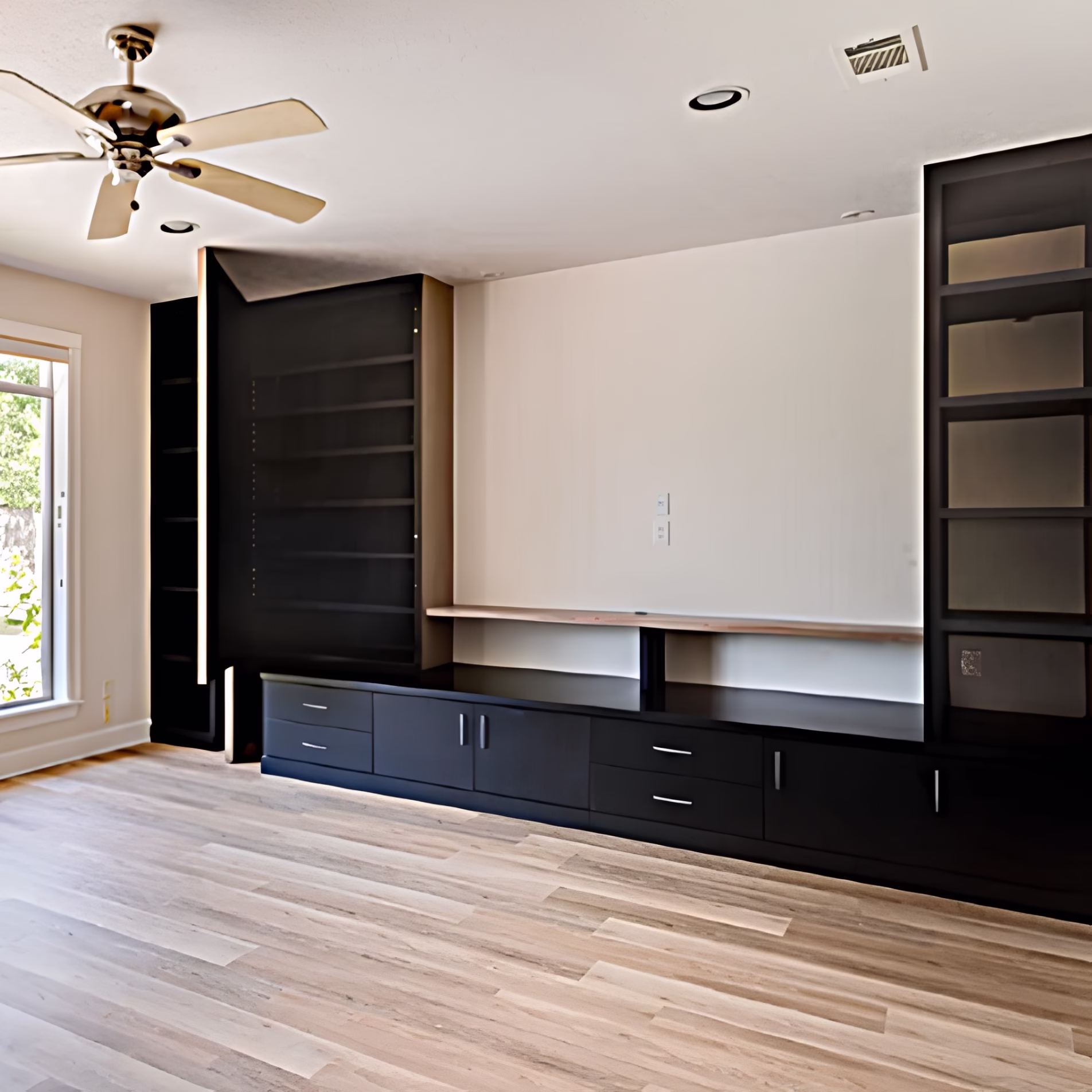 Custom living room built-ins with black shelving, lower cabinets, drawers, and a concealed storage door.