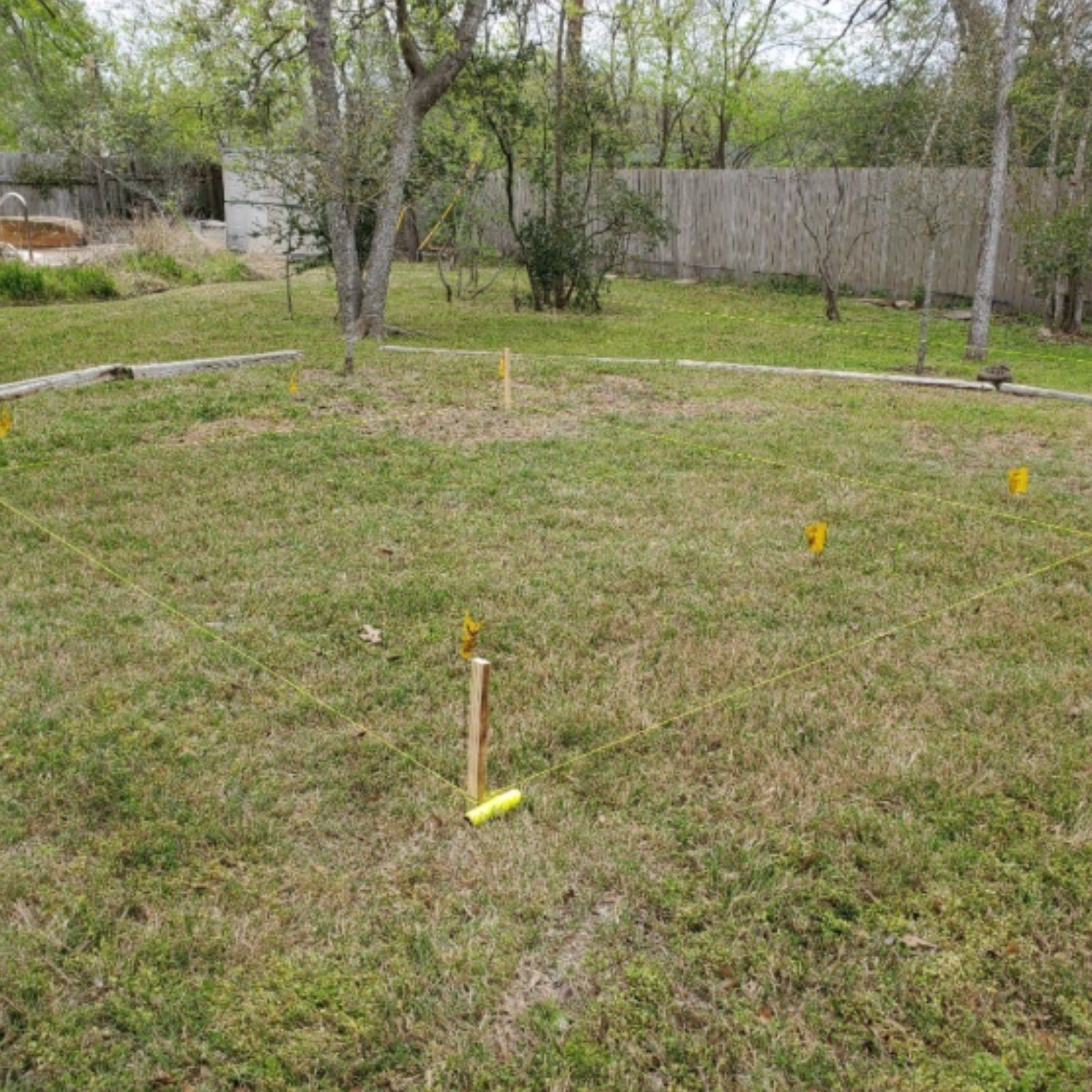 Stakes and string marking the planned footprint of a detached home office in a wooded backyard.