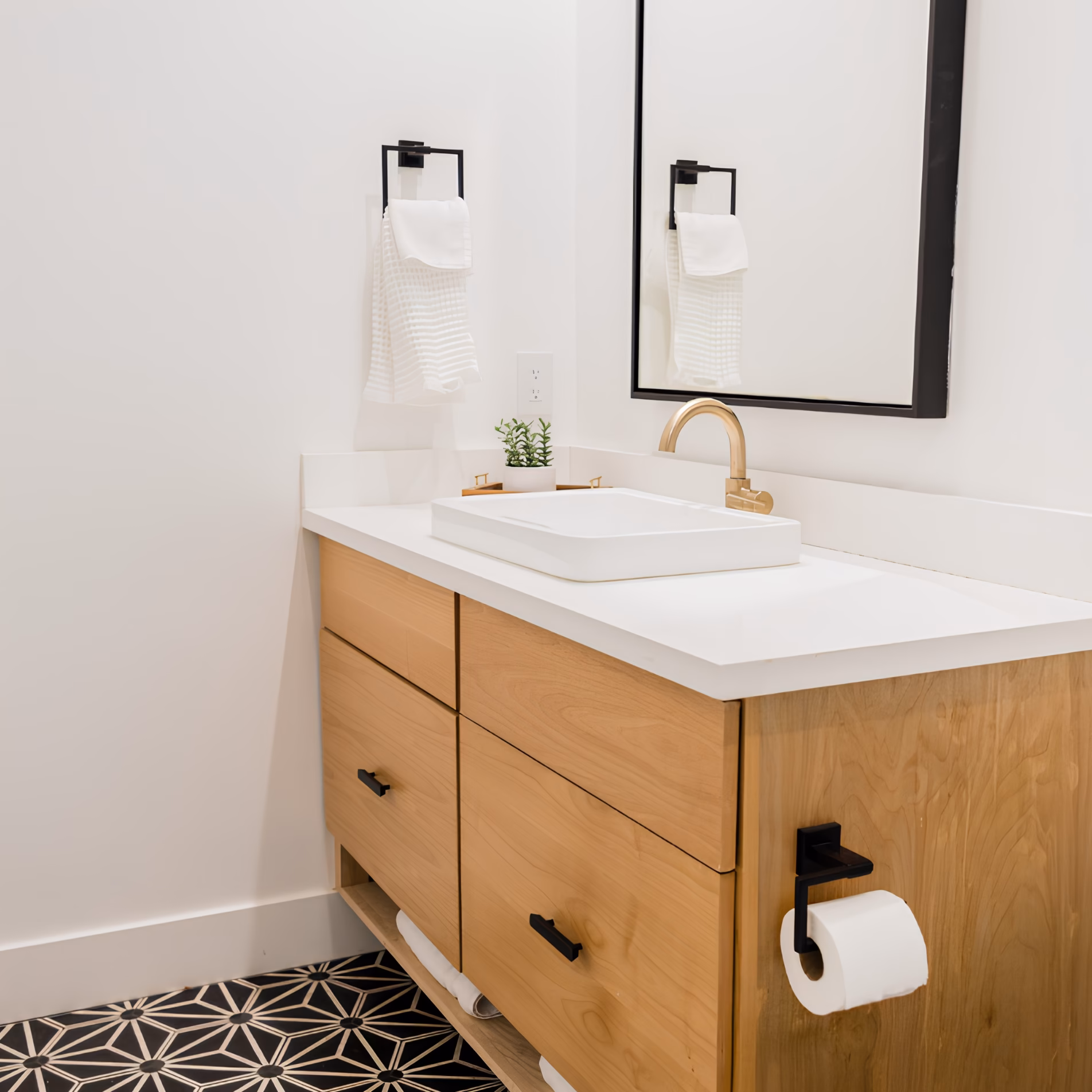 Bathroom vanity with a gold faucet, black cabinet hardware, black-framed mirror, and matching black towel accessories.