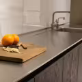 Stainless steel countertop beside a wooden cutting board with oranges and spices in a contemporary kitchen.