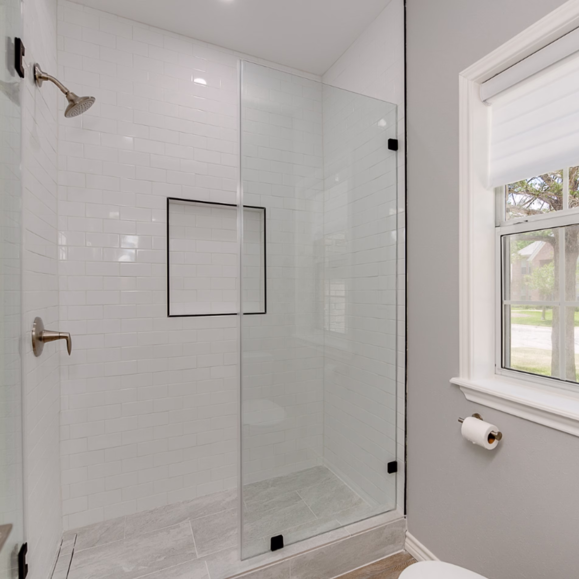 White subway tile shower with light grout creating a subtle tile pattern behind a glass enclosure.