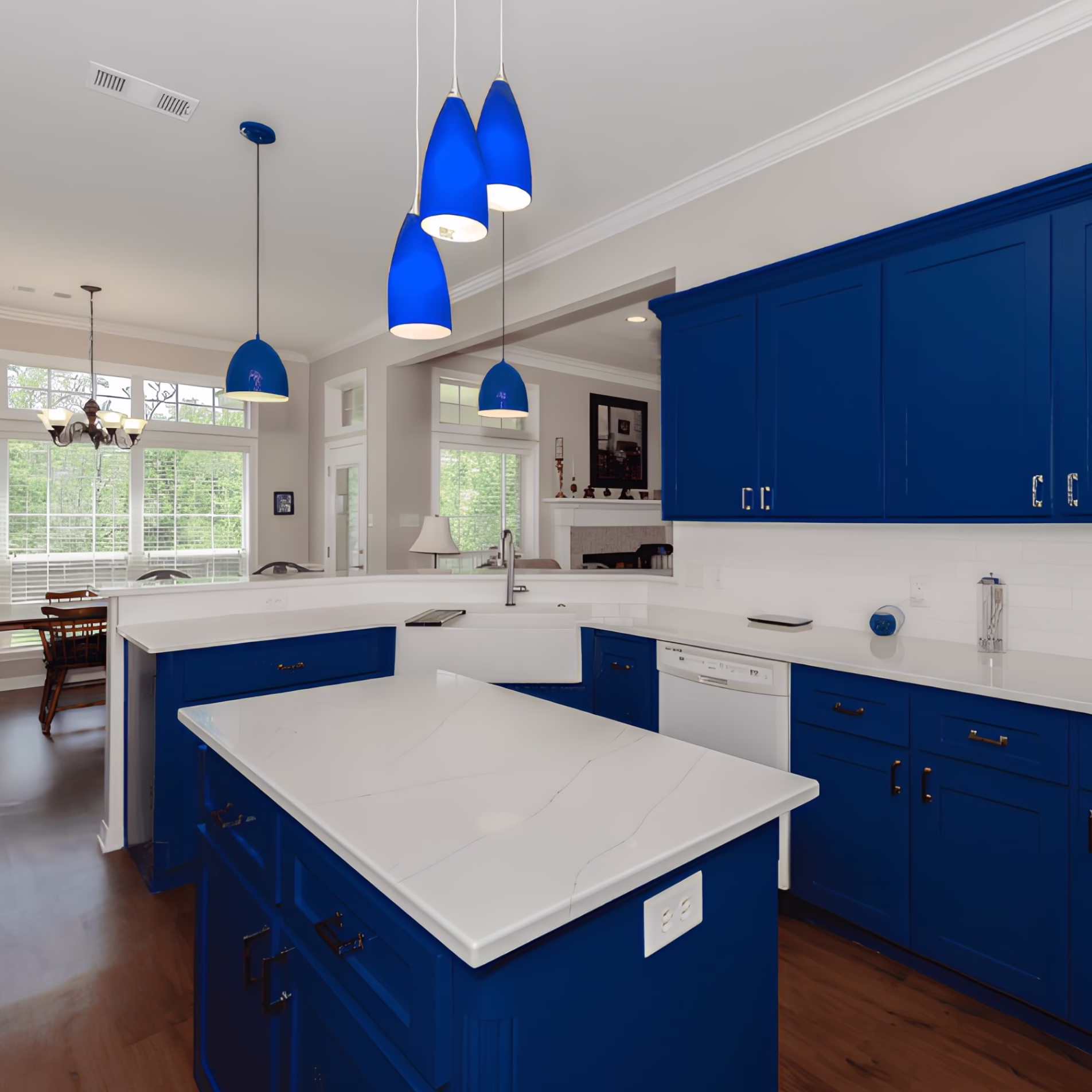 Kitchen with bright blue cabinetry, white countertops, and five blue pendant lights suspended above the island and sink area.