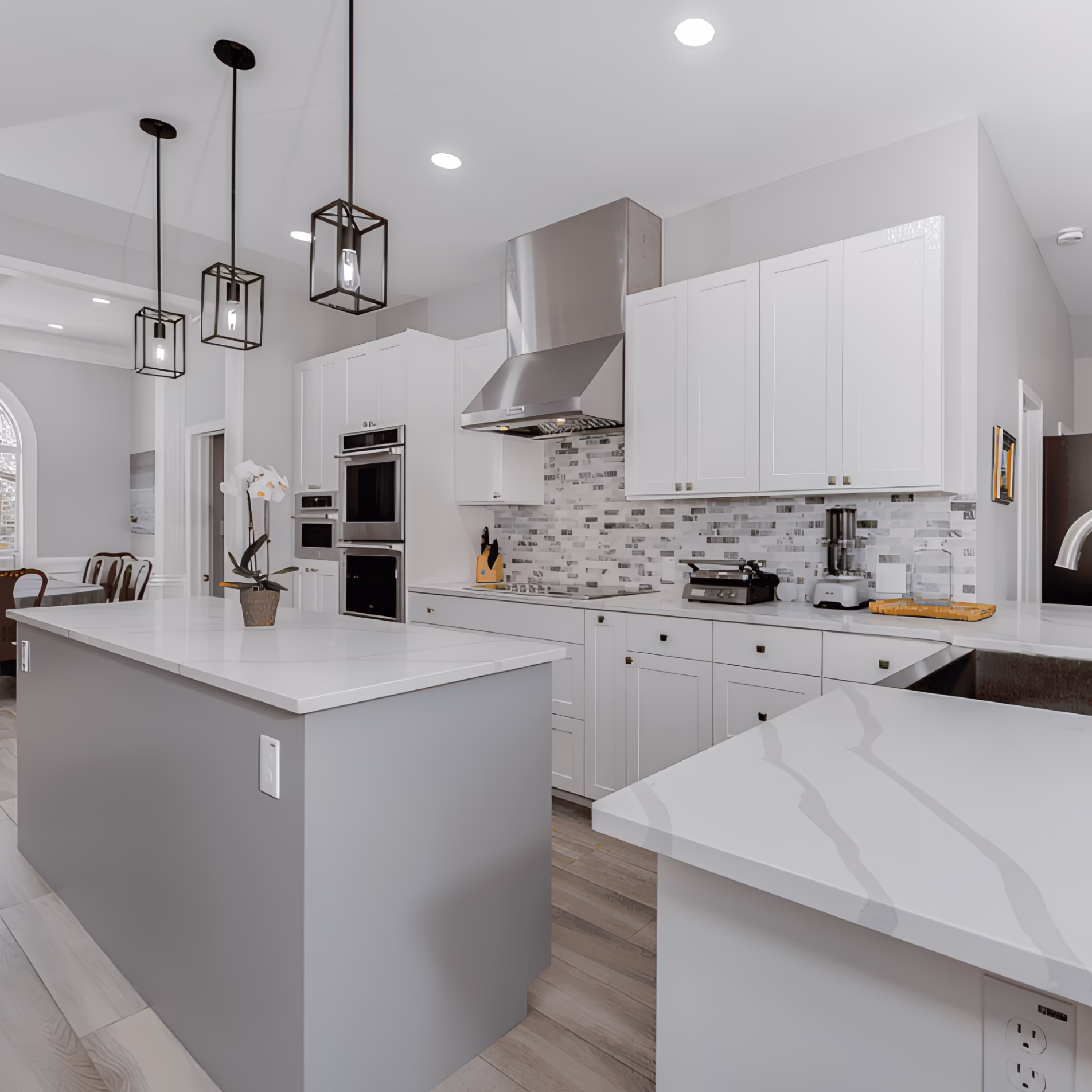 White kitchen with black-framed pendant lights above the island, recessed ceiling lights, and a stainless steel range hood with integrated lighting.