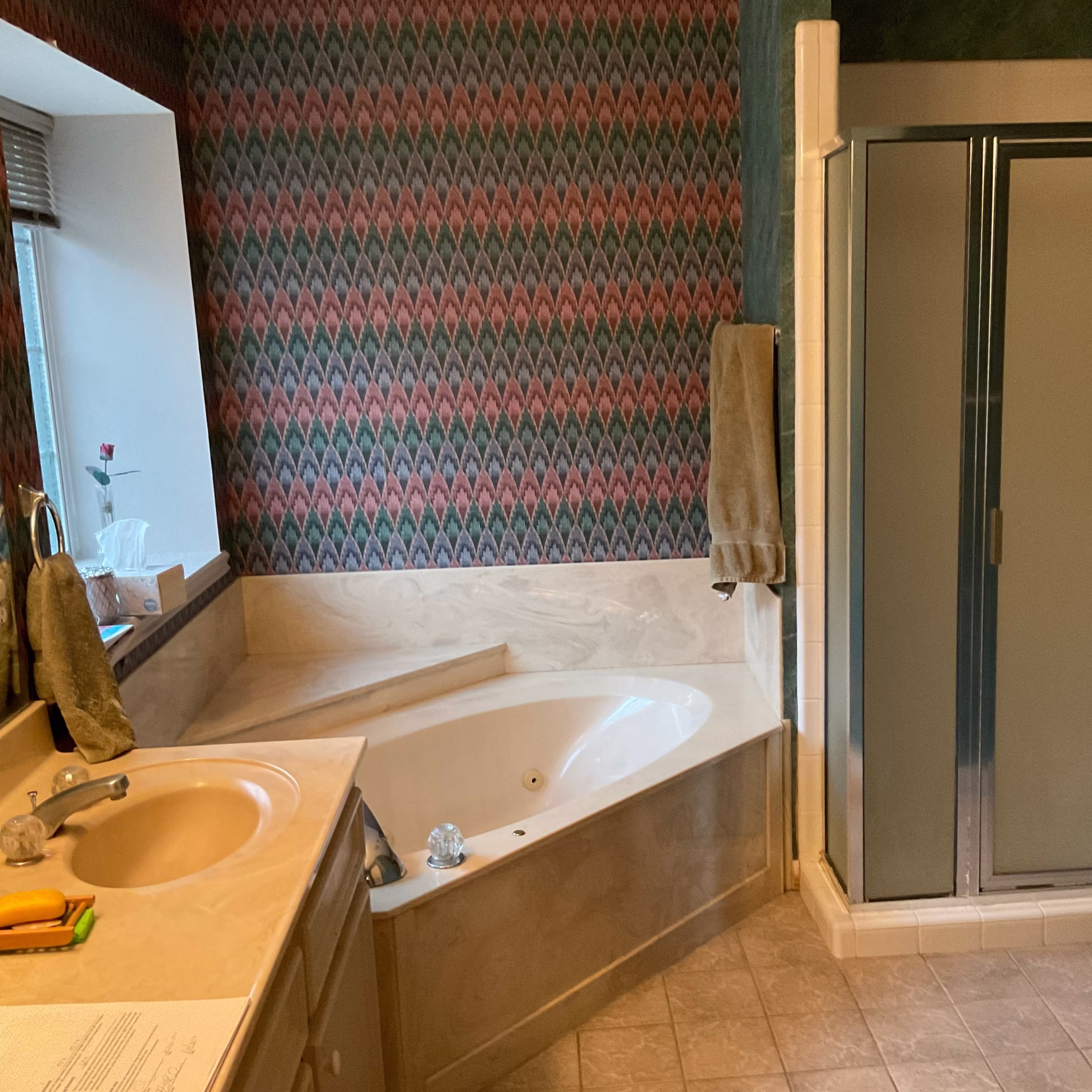 Primary bathroom before remodeling with an oversized corner jetted tub, small enclosed shower, and patterned wallpaper