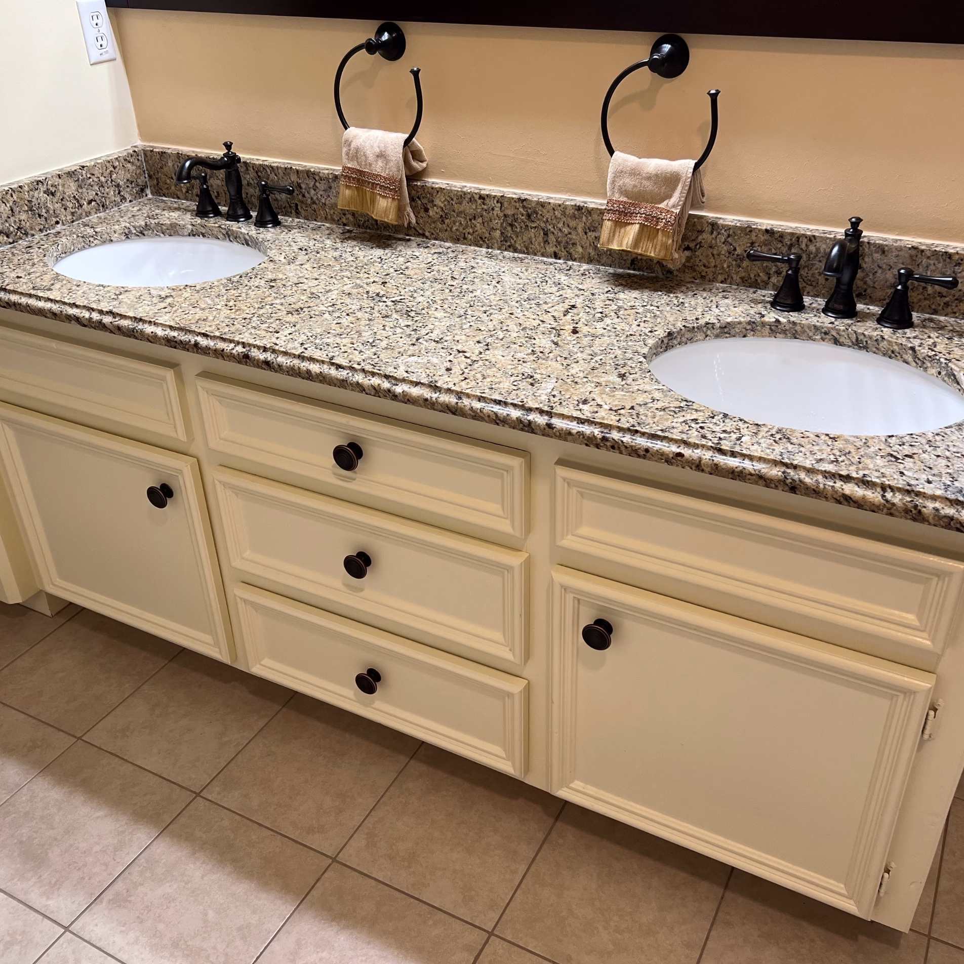 Updated double vanity with Venetian gold granite countertop, white sinks, dark faucets, and painted off-white cabinets