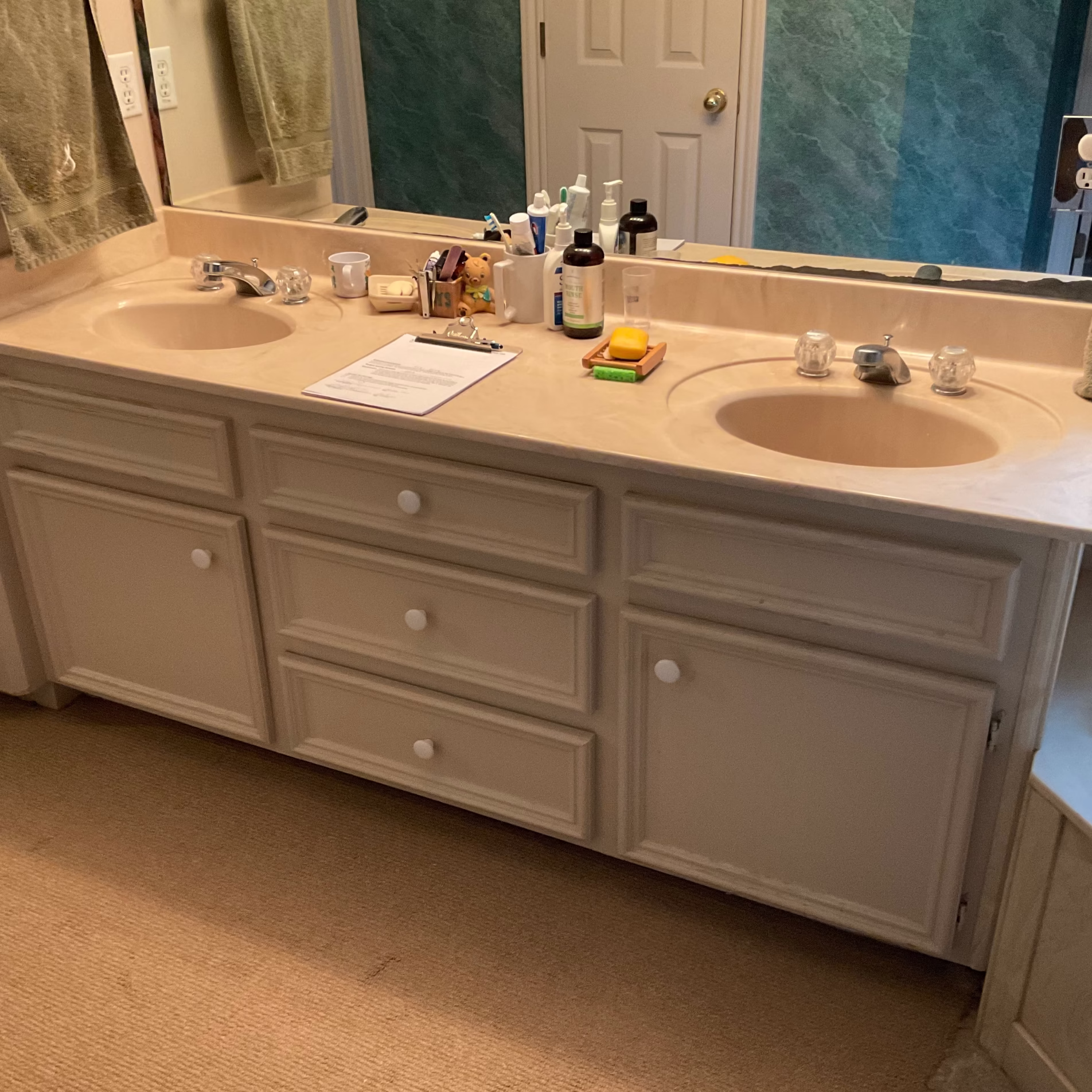 Original primary bathroom vanity with beige countertop, inset sinks, clear knob faucets, and white cabinetry