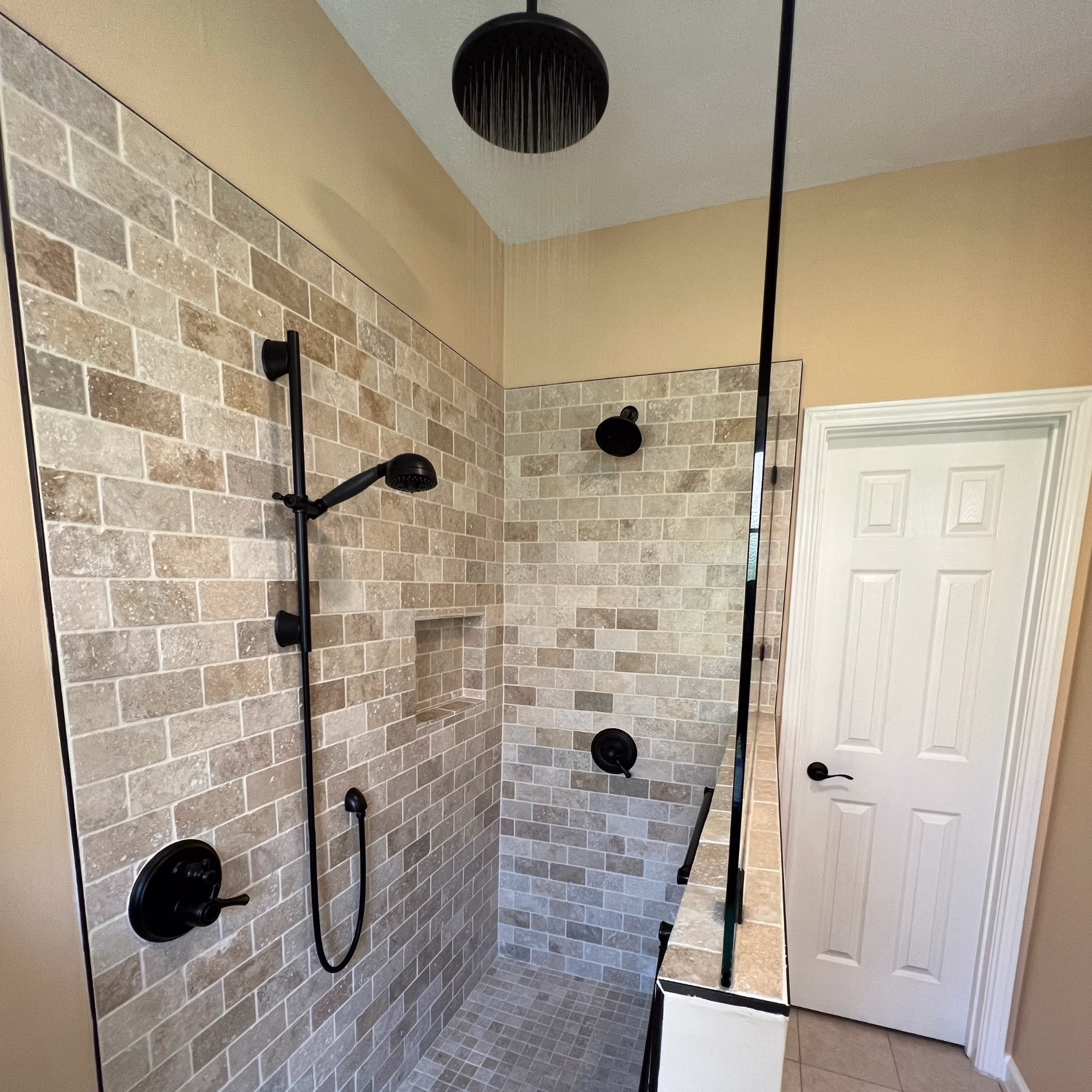 Finished aging-in-place bathroom with tumbled travertine shower, multiple showerheads, built-in niche, grab bars, and lever door handle