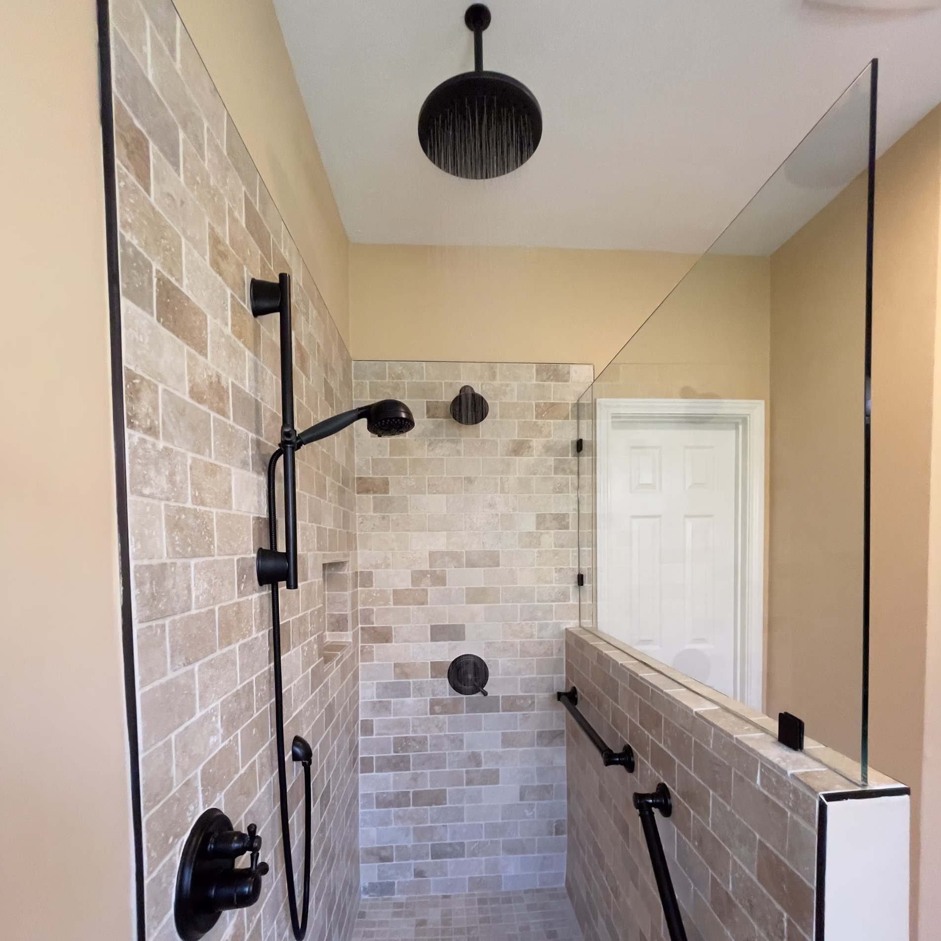 Accessible tiled shower with handheld showerhead, rainfall showerhead, built-in niche, grab bars, and glass partition