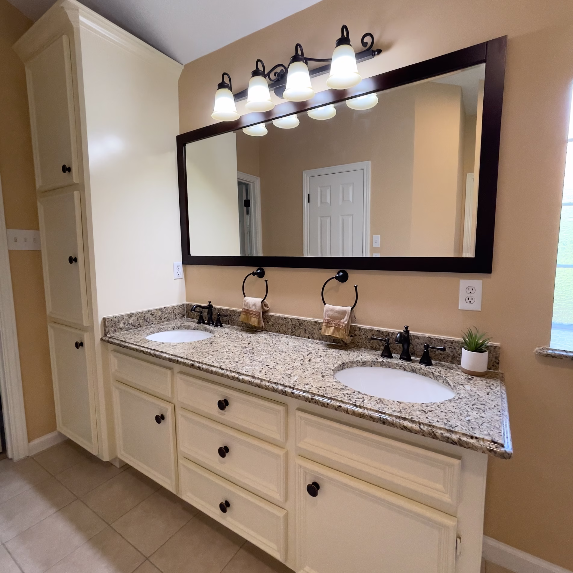 Remodeled double vanity with Venetian gold granite, off-white cabinetry, framed mirror, and updated lighting
