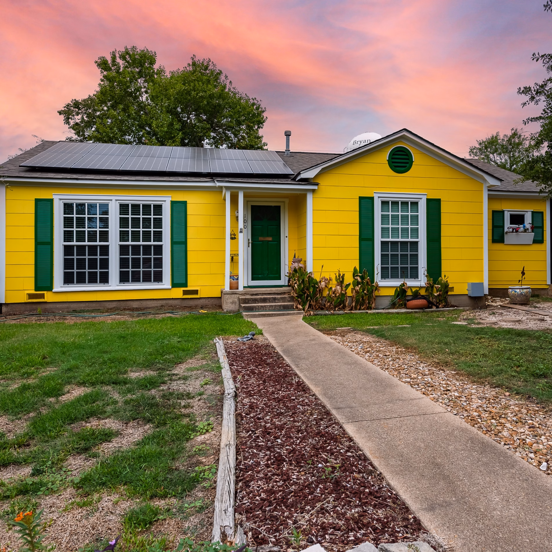 Bright yellow exterior of a remodeled 1950s home in Bryan, Texas, with green shutters, white trim, and a green front door.