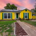 Bright yellow exterior of a remodeled 1950s home in Bryan, Texas, with green shutters, white trim, and a green front door.