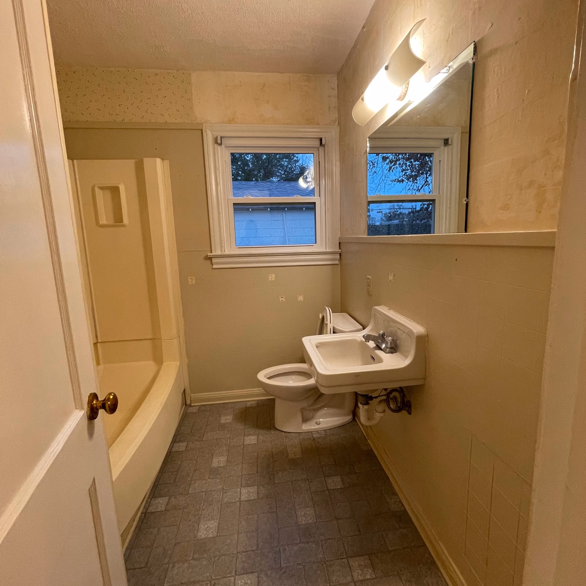Guest bathroom before remodeling, featuring a prefabricated bathtub and shower, original wall-mounted sink, and gray tile flooring.