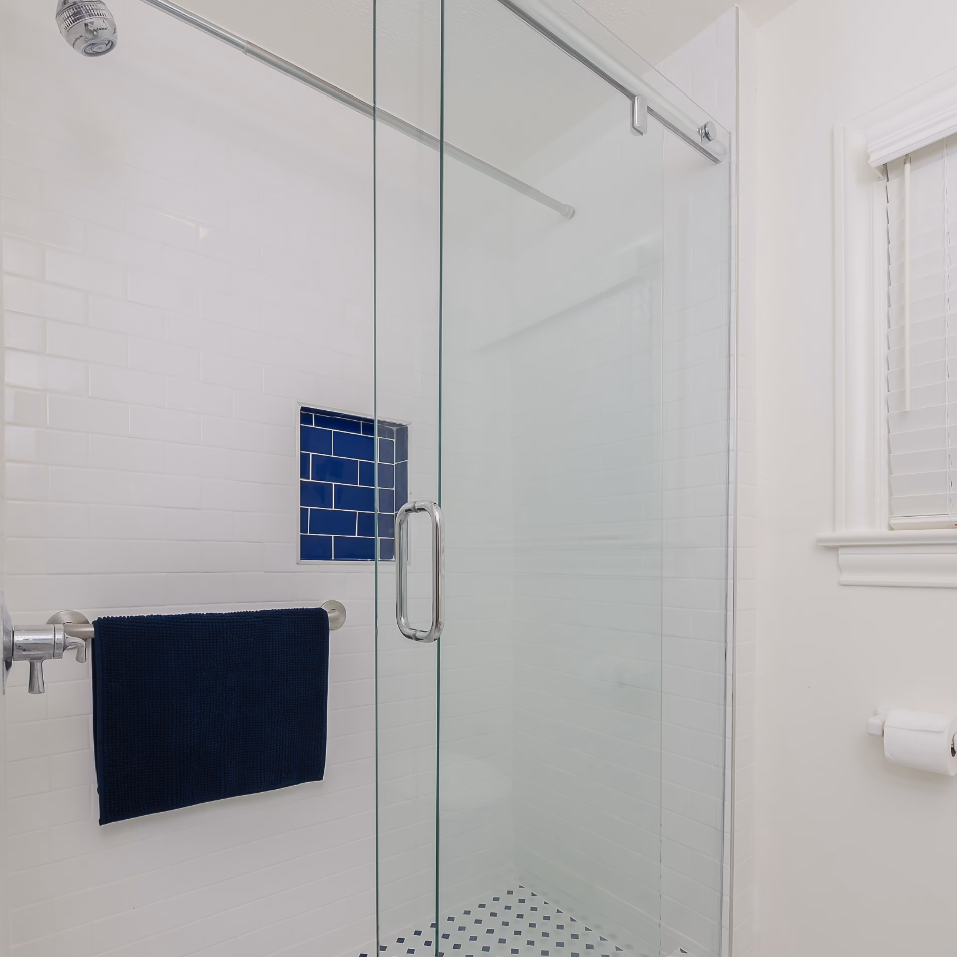 New walk-in shower with white subway tile, blue-tiled wall niche, sliding glass door, and blue-and-white patterned shower floor.