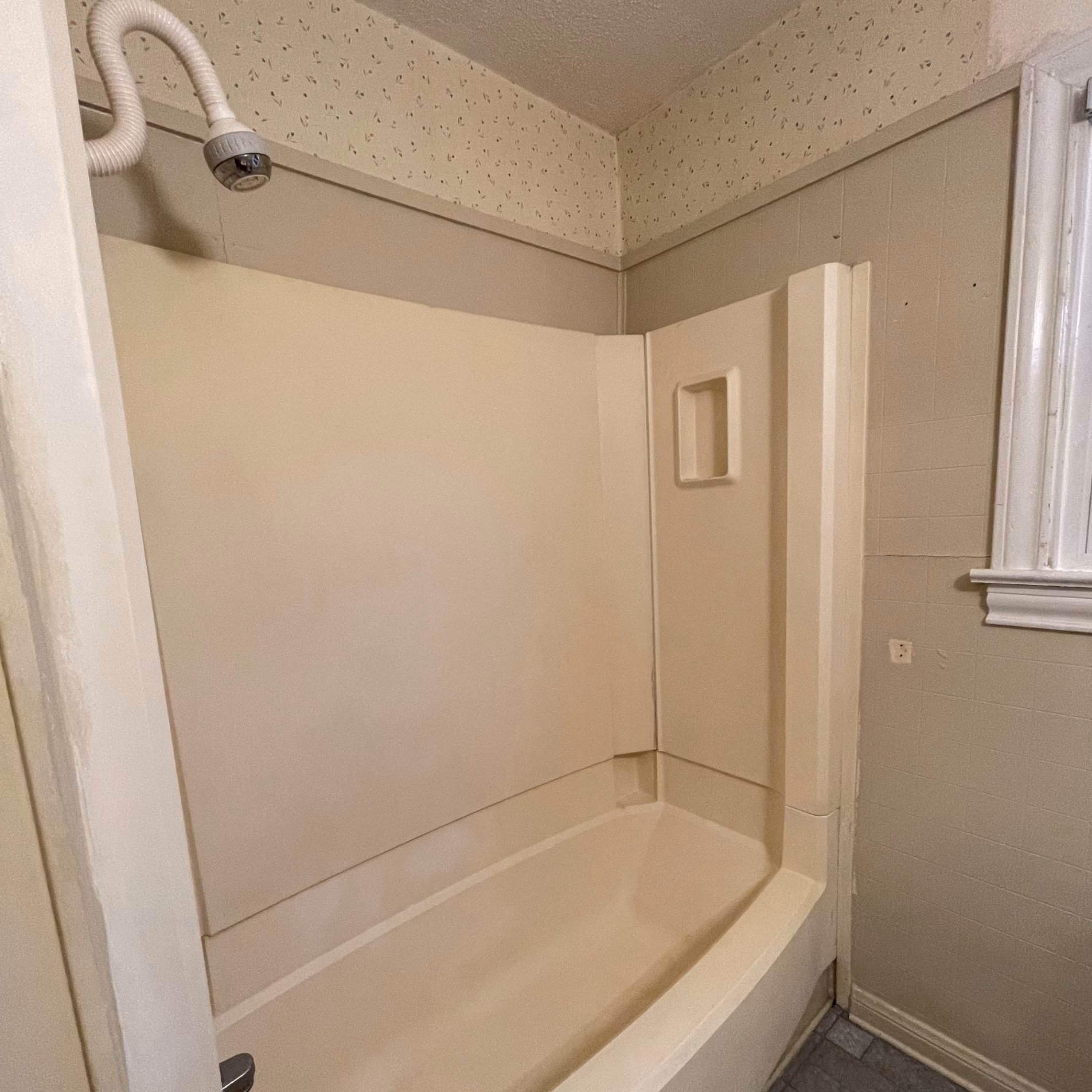 Original prefabricated bathtub and shower combination with built-in soap niche before the guest bathroom remodel.