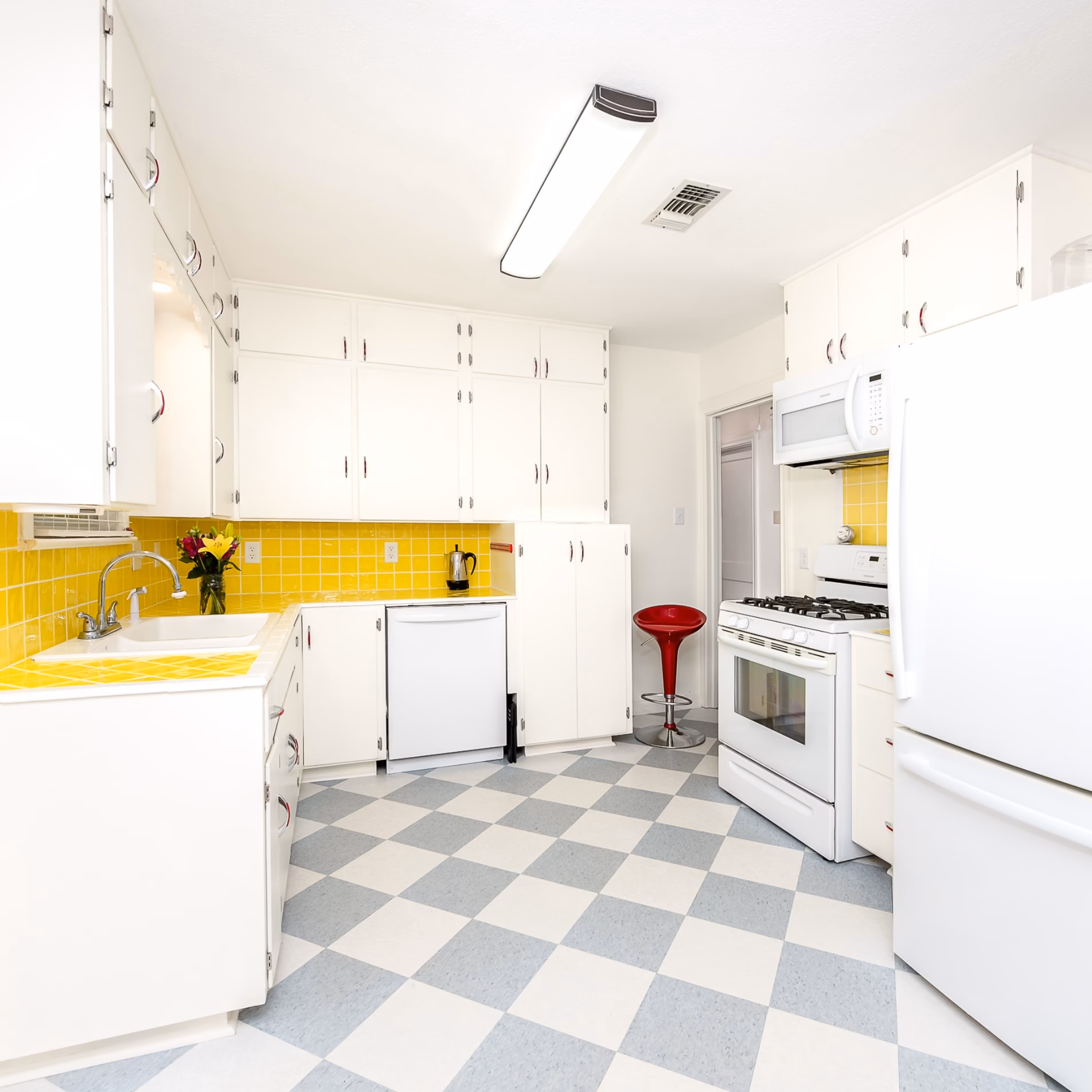 Wide view of remodeled vintage kitchen with yellow tile backsplash, white cabinetry, new dishwasher, and gray-and-white checkerboard flooring.