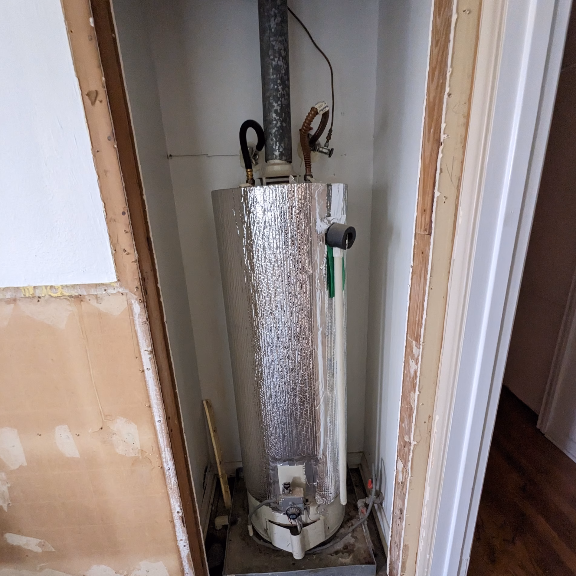 Original tank-style water heater located inside a narrow closet before replacement with an exterior tankless unit.
