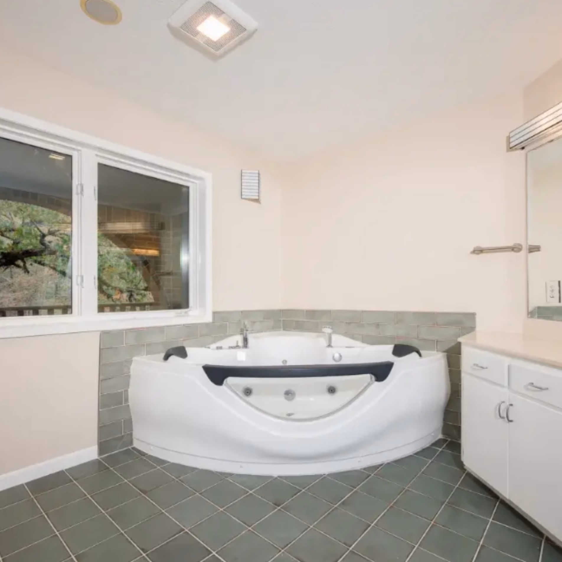 Remodeled Gibb Estates bathroom featuring a white jetted corner bathtub, green tile surround, and matching green floor tiles.