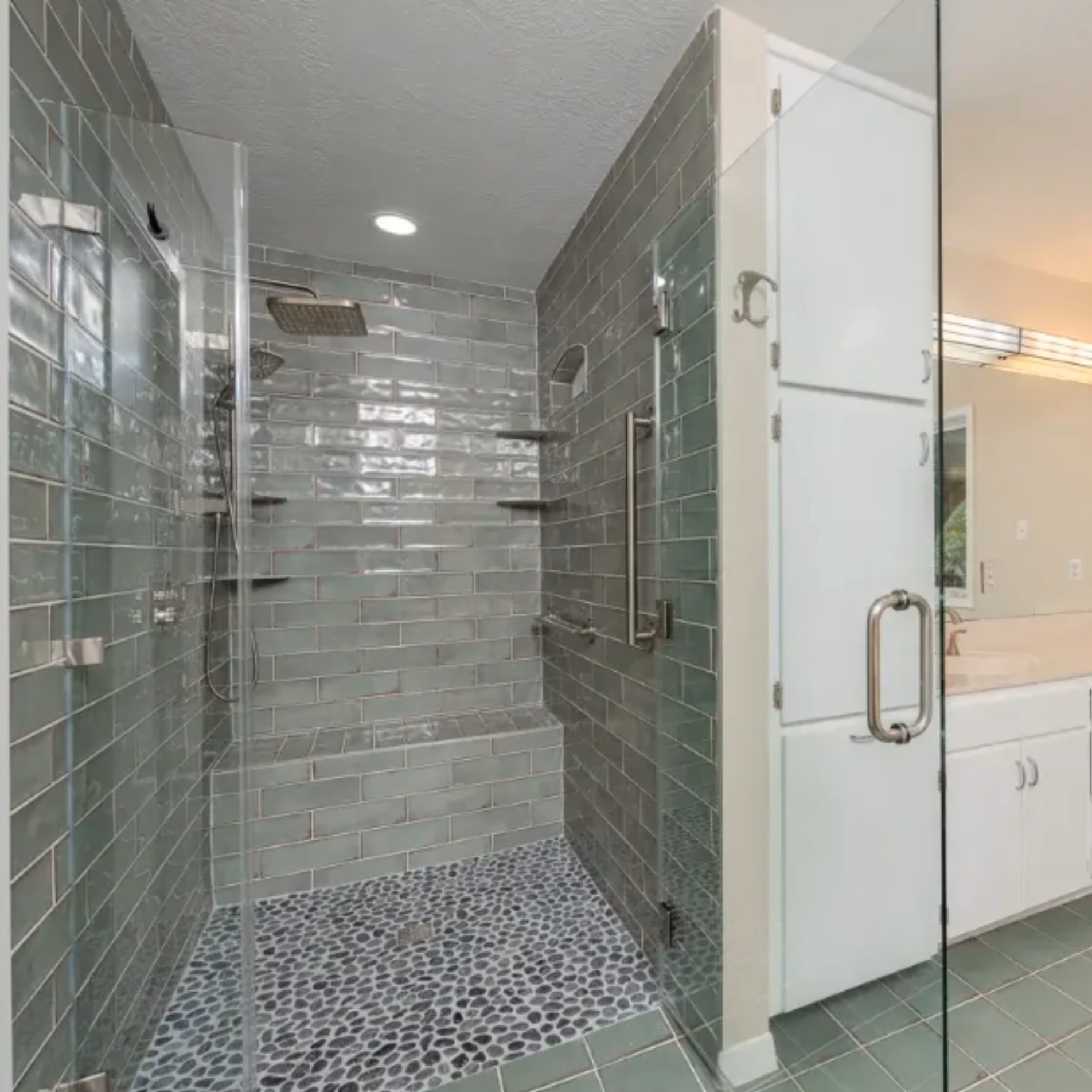 Completed aging-in-place bathroom remodel in College Station featuring a curbless shower with green wall tiles, pebble flooring, and grab bars.