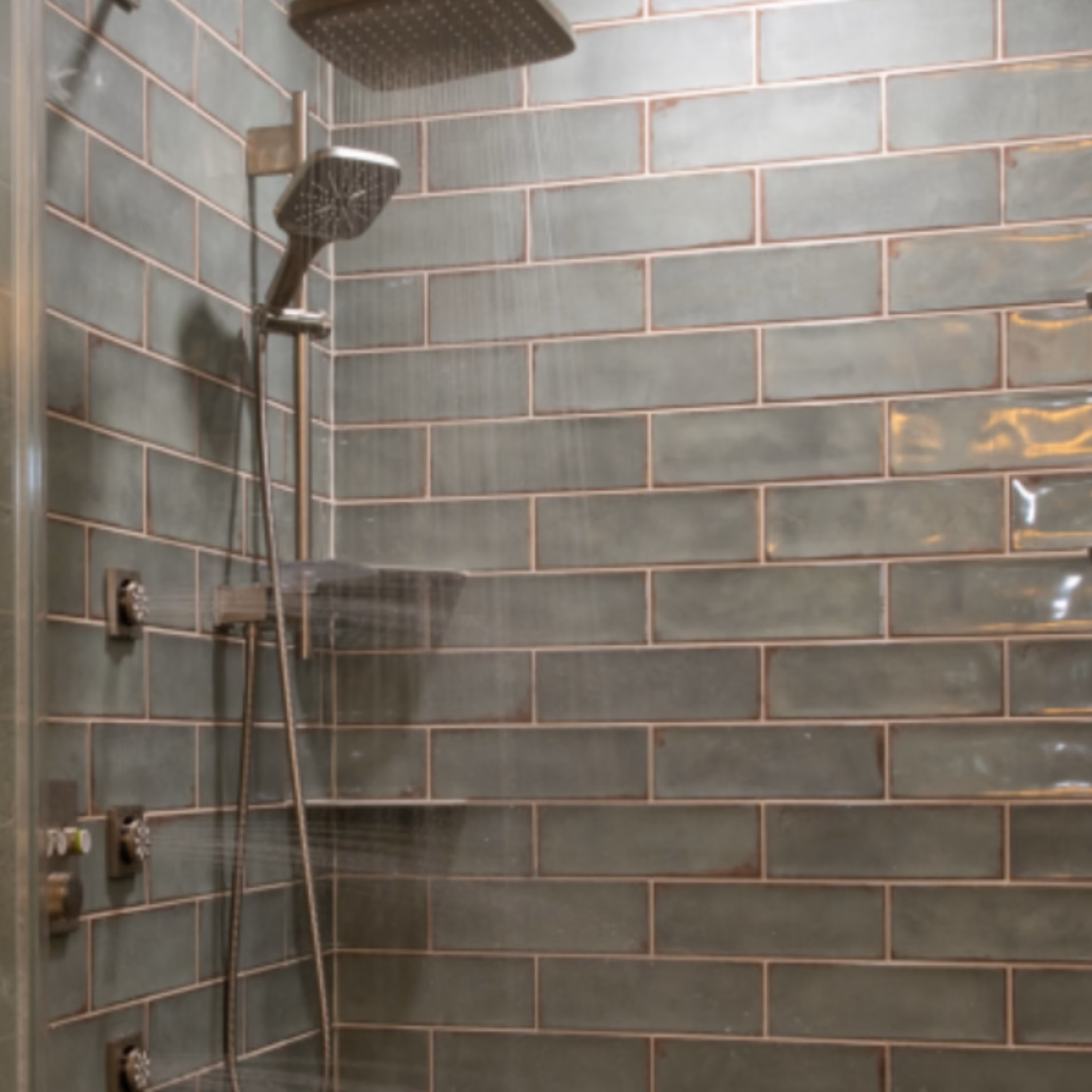 Close-up of rainfall and handheld showerheads against green subway tile walls in the remodeled Gibb Estates bathroom.