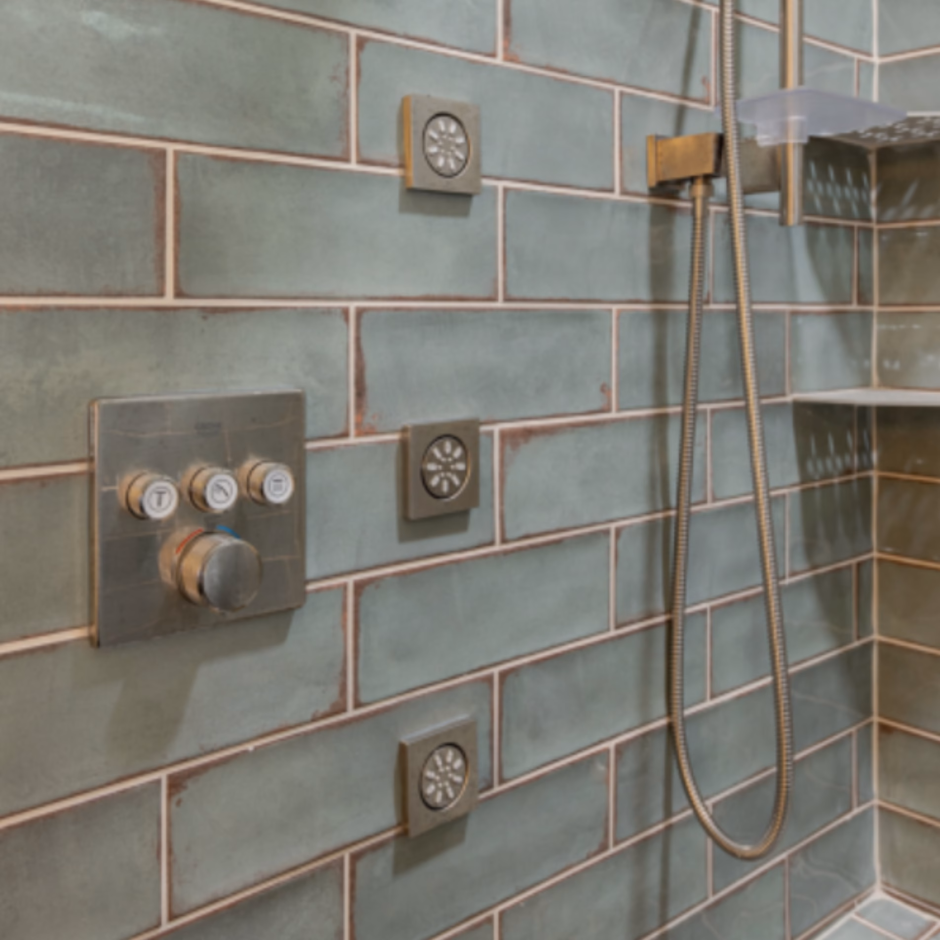 Close-up of satin nickel shower controls and body jets installed against nature-inspired green subway tiles.