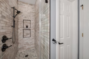 Walk-in shower with pebble tile flooring and neutral stacked tile walls completed during a guest bathroom makeover