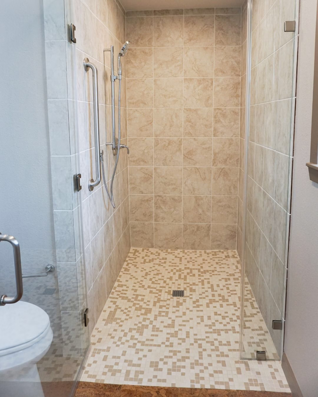 Curbless walk-in shower completed during aging in place renovation with grab bars and smooth floor transition.