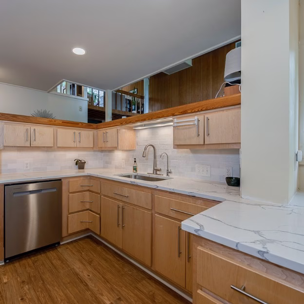 corner kitchen view from a mid century modern home renovation in College Station showing quartz countertops, wood cabinetry, and open layout to adjacent living space