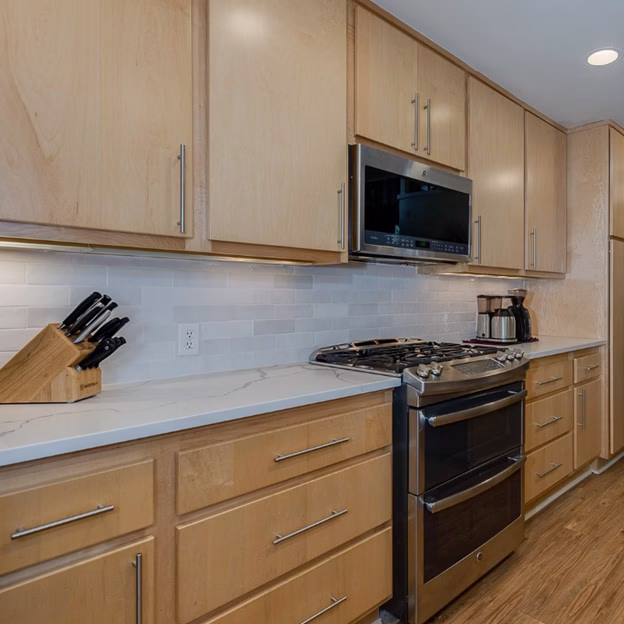 mid century modern remodel College Station kitchen after with light wood cabinets, white quartz countertops, and simple white tile backsplash at the range