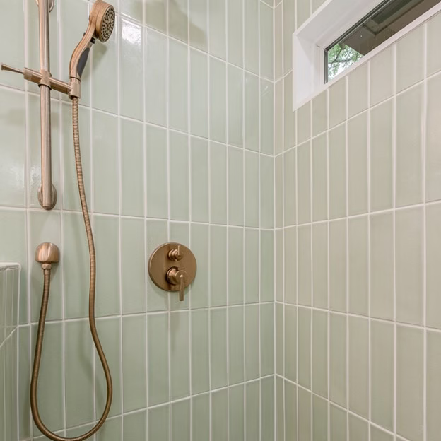 green tile shower from mid century modern bathroom remodel College Station with vertical stacked tile, brass fixtures, and added transom window for natural light