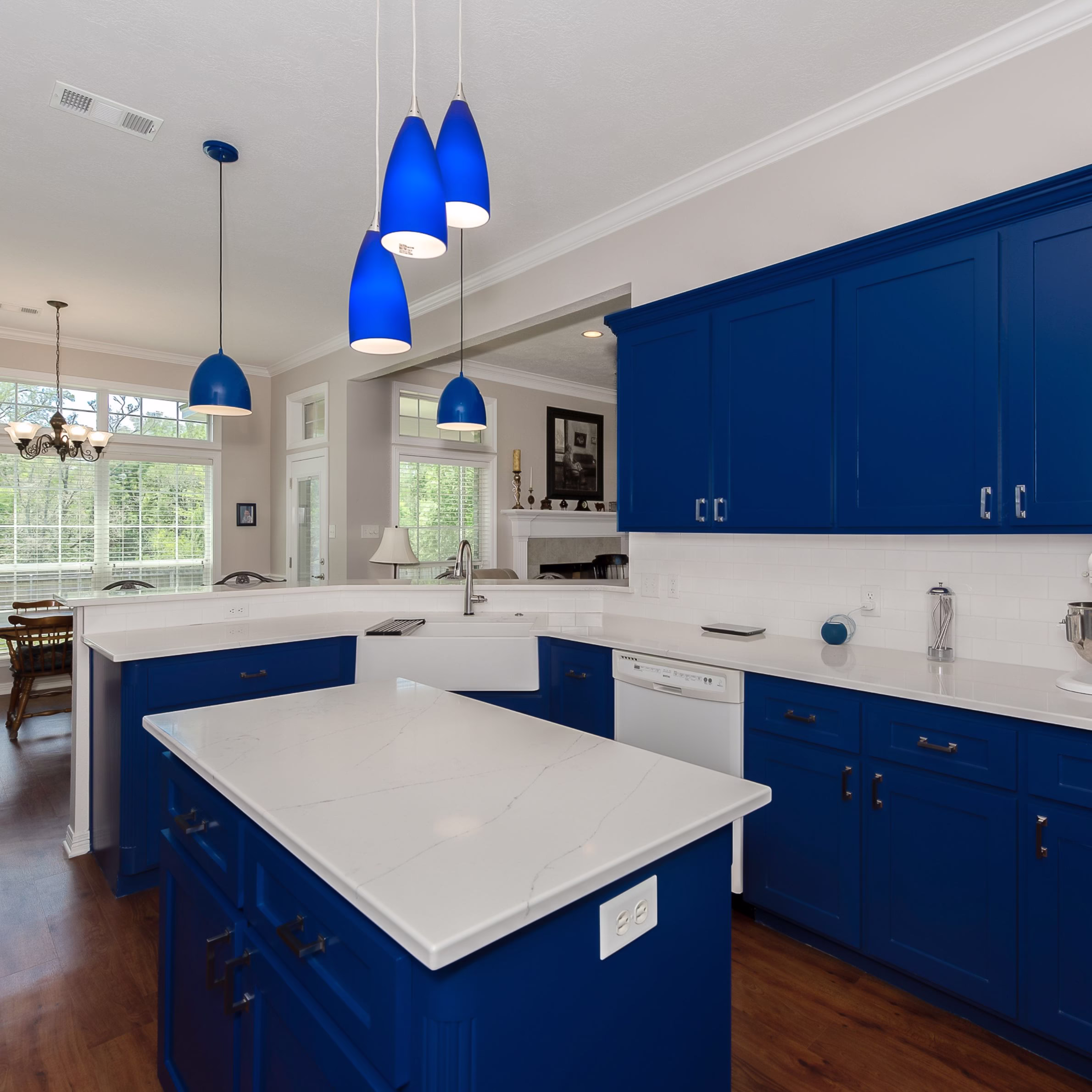 Renovated kitchen with custom blue cabinetry, white quartz surfaces, workstation sink, and modern lighting completed during a whole home renovation Bryan TX.